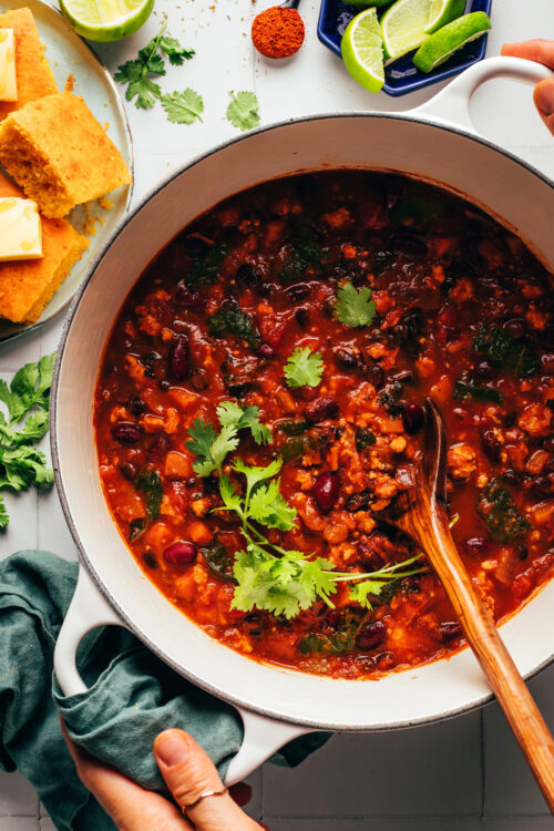 Hands holding the handles of a Dutch oven of pumpkin turkey chili