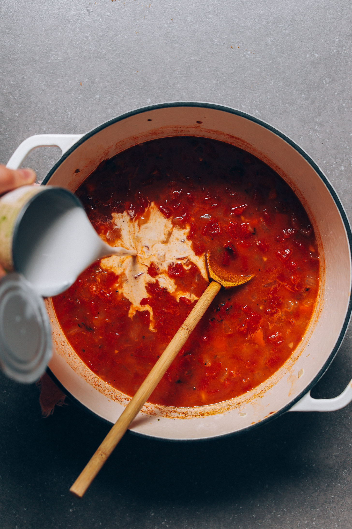 Pouring coconut milk into a soup pot for our creamy dairy-free Pumpkin Black Bean Soup recipe