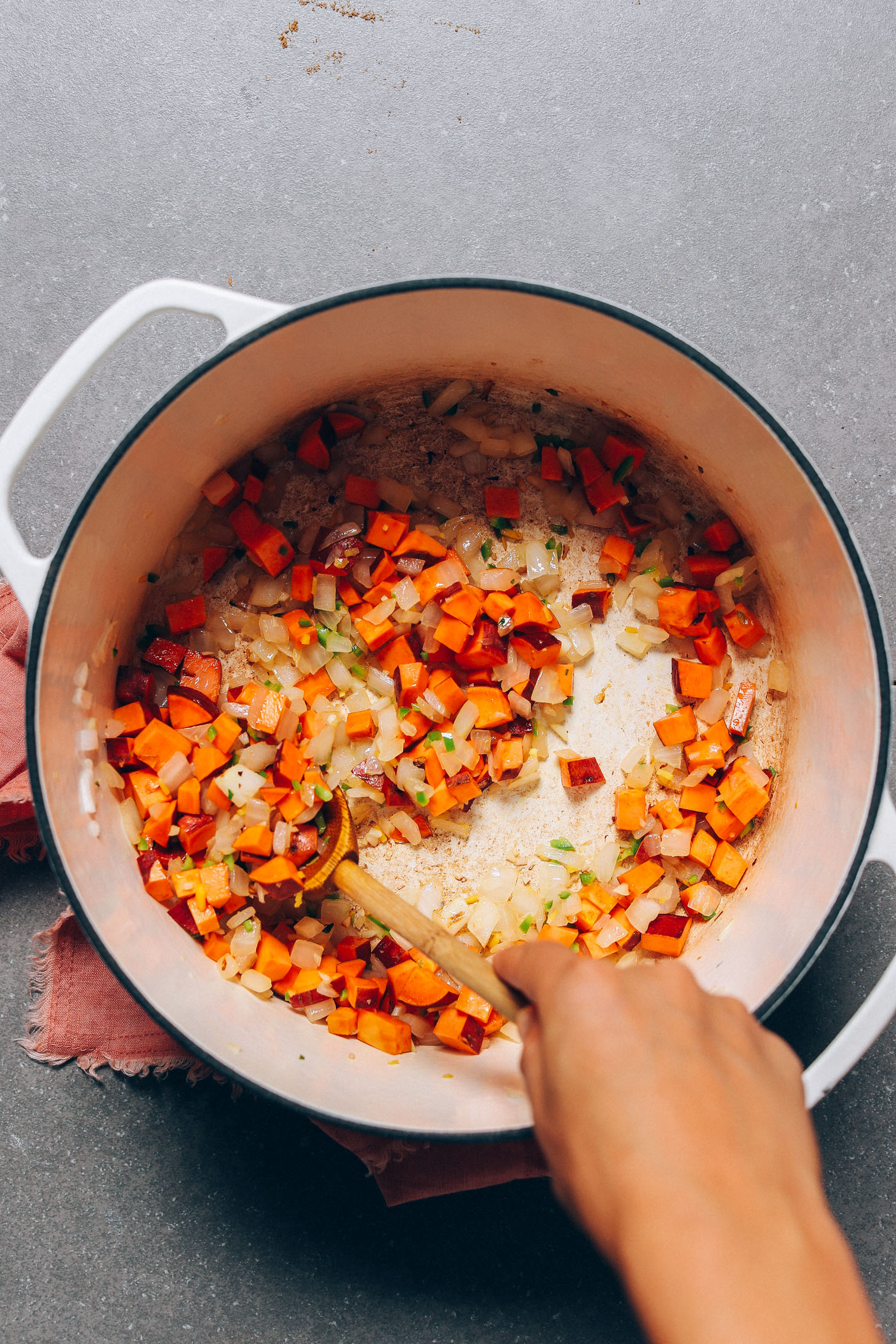 Using a wooden spoon to stir sweet potatoes, onion, and seasonings for our Black Bean Pumpkin Soup recipe