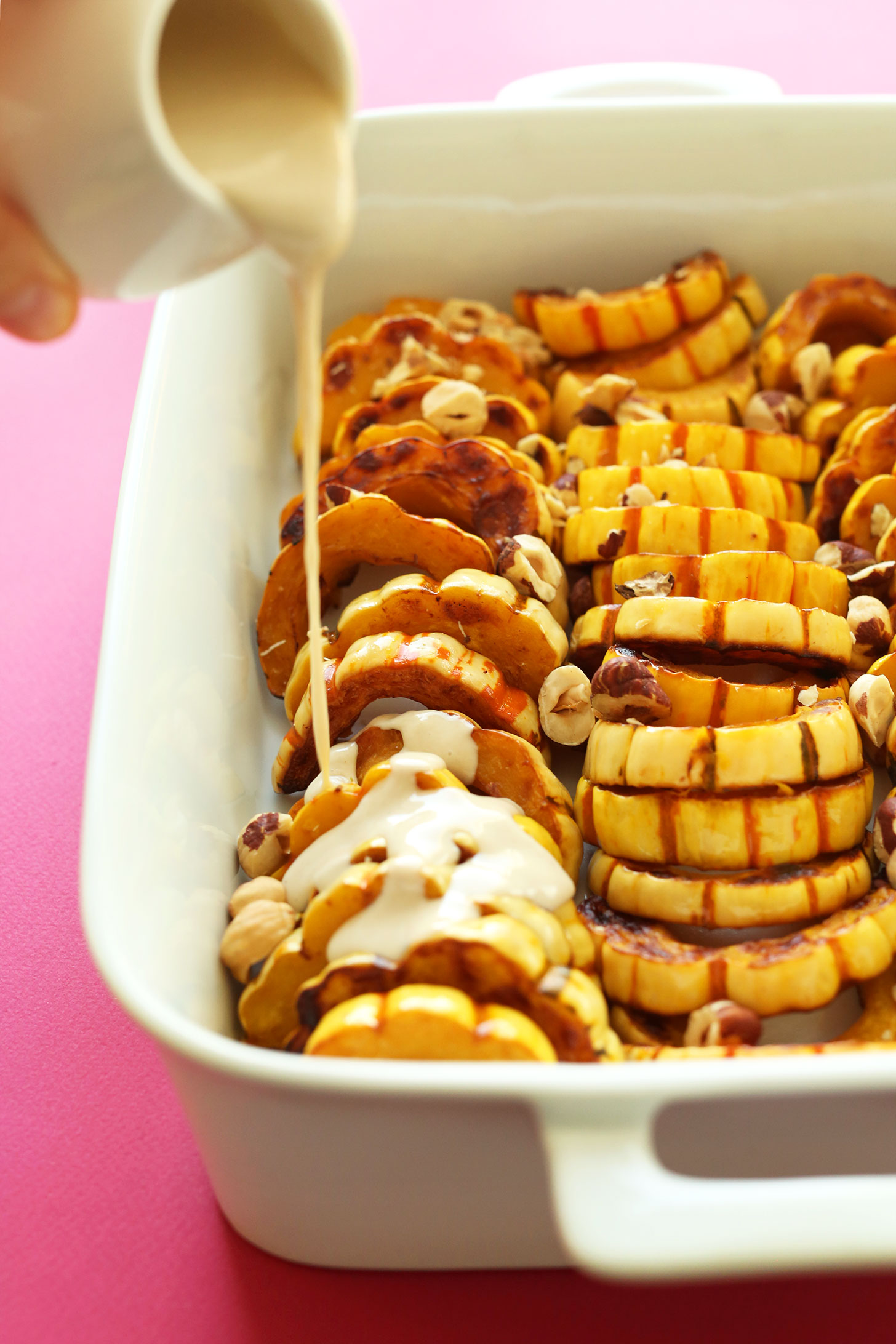 Pouring tahini sauce over our Delicata Squash Bake recipe