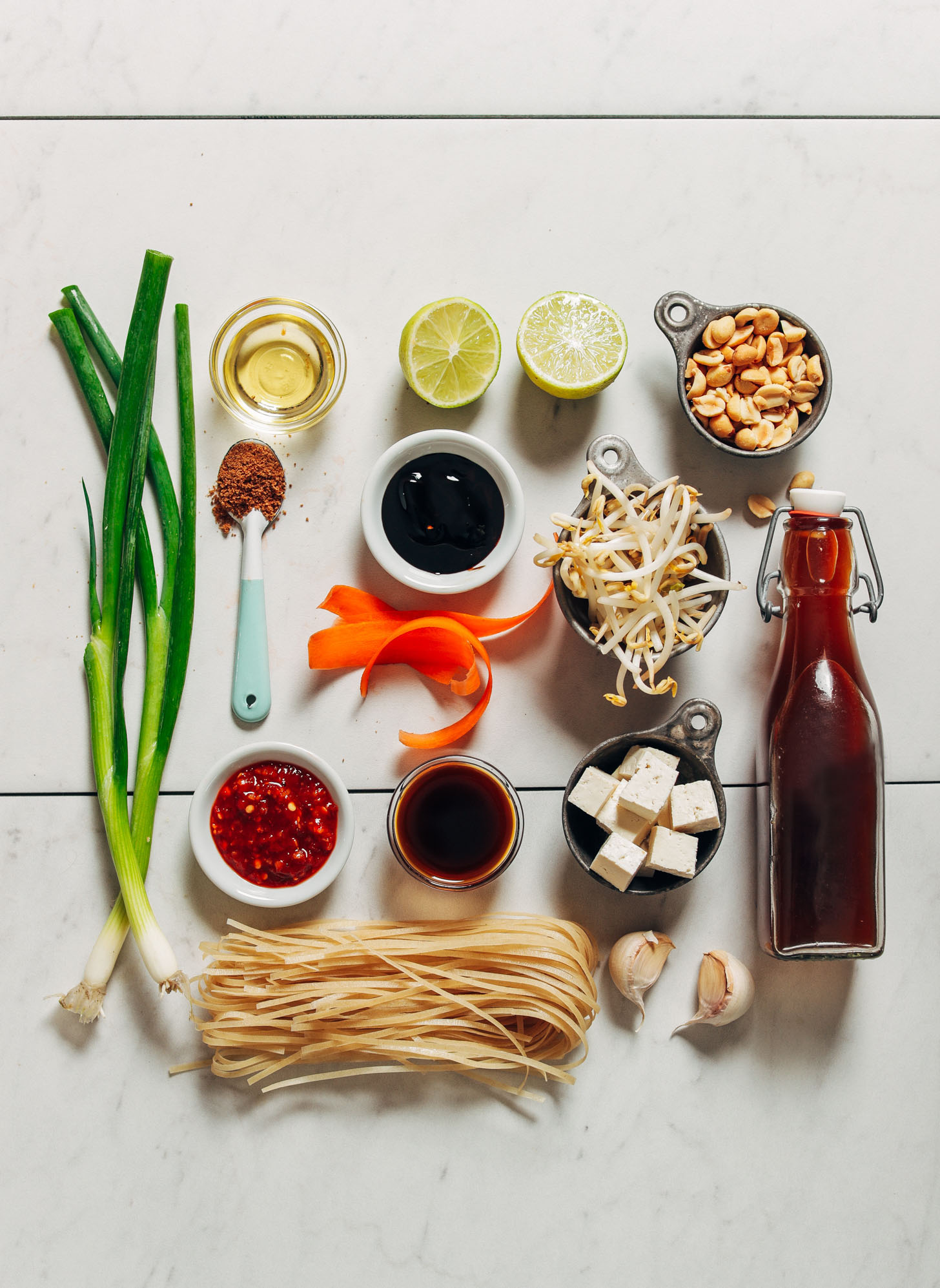 Bird's eye view image of green onion, chili sauce, peanuts, bean sprouts, and other ingredients for making pad thai