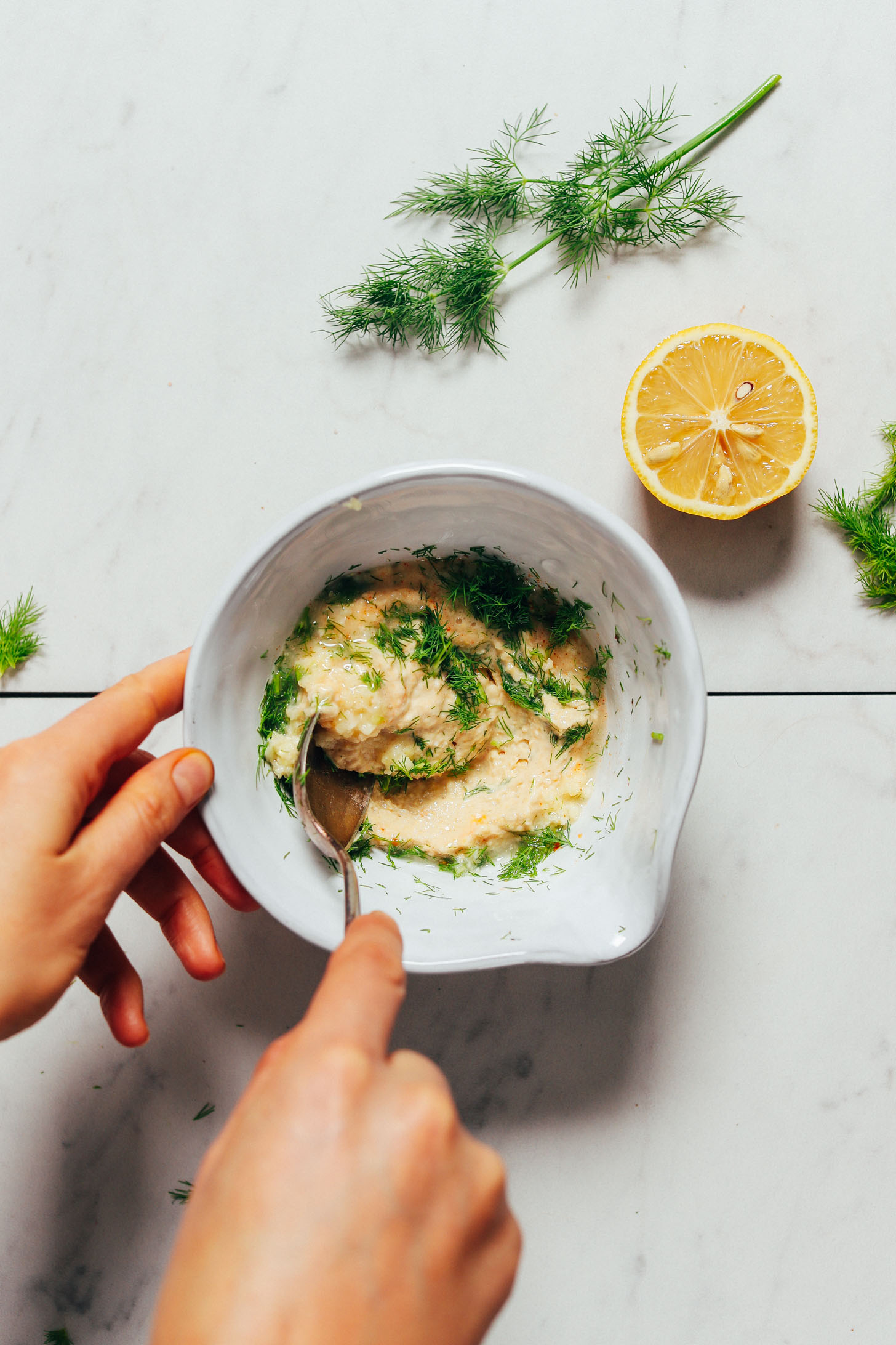 Using a spoon to stir a bowl of our easy Garlic Dill Sauce for topping salads, bowls, and more