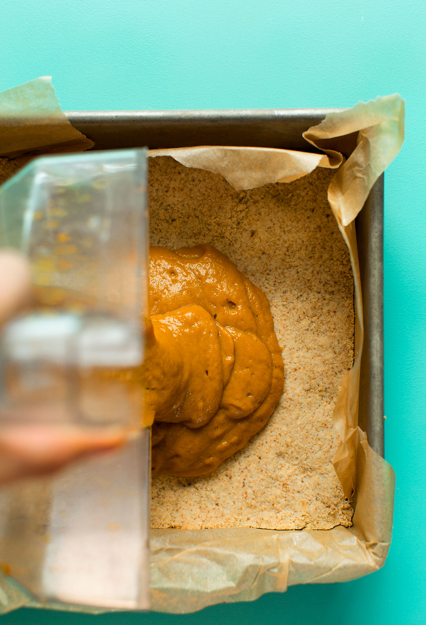 Pouring vegan pumpkin pie bar filling over gluten-free crust for a Thanksgiving dessert