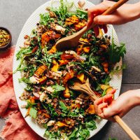 Using wood serving spoons to pick up a serving of roasted squash salad