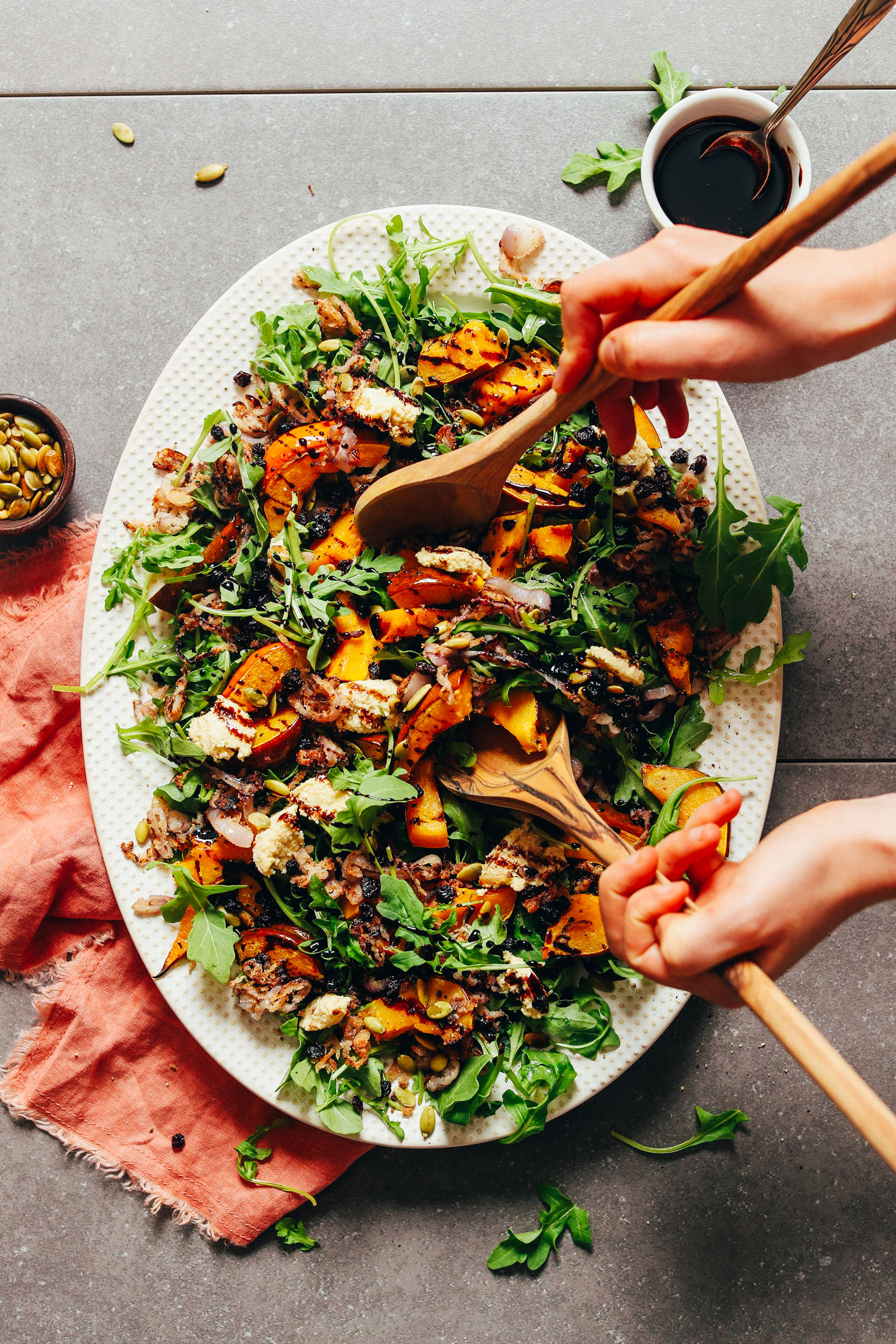 Using wood serving spoons to pick up a serving of roasted squash salad