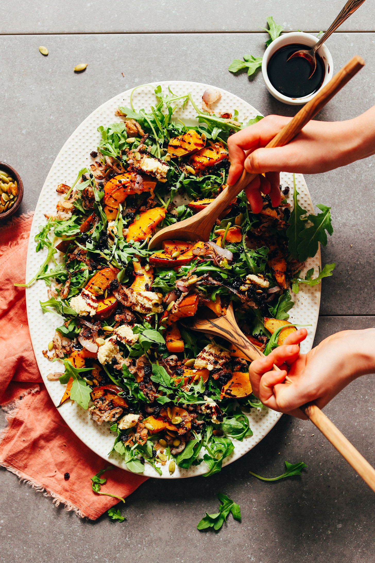 Using salad tongs to grab a serving of Roasted Squash Salad with Nut Cheese and Balsamic Reduction