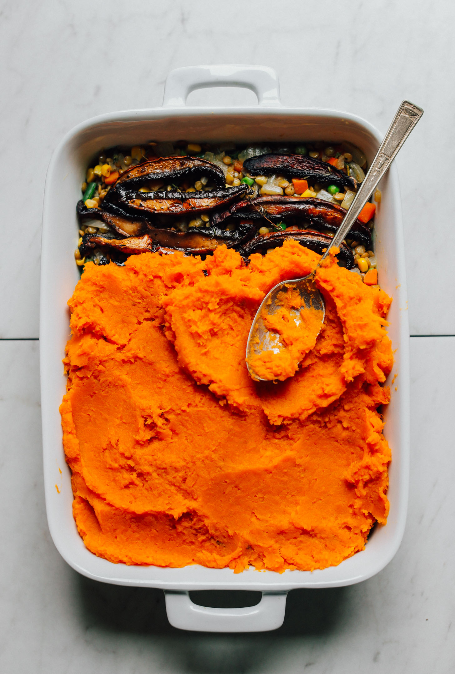 Ceramic baking dish containing Sweet Potato Lentil Shepherd's Pie with the bottom layer partially exposed to reveal it's hearty nature