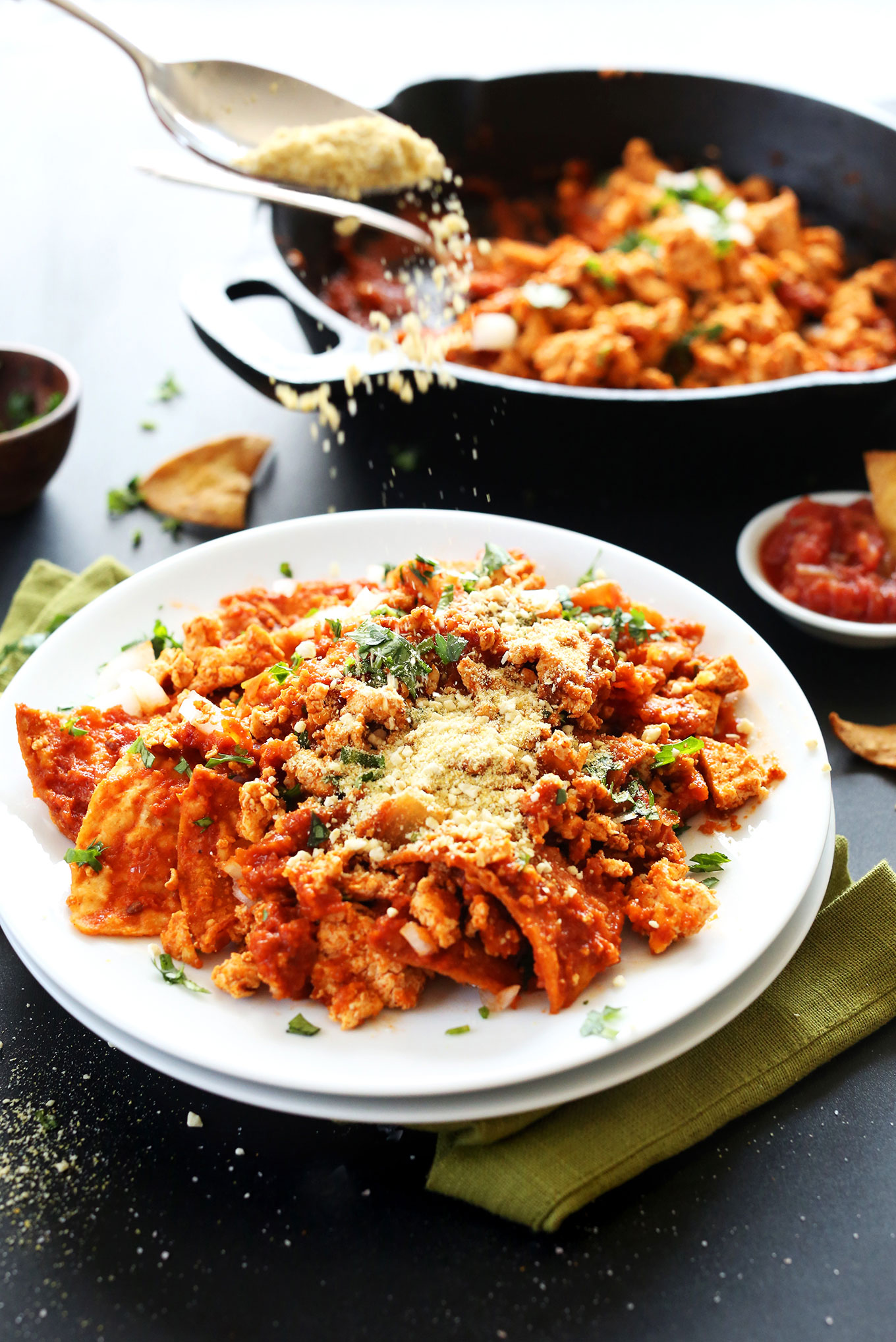 Sprinkling vegan parmesan over Tofu Chilaquiles made with baked chips