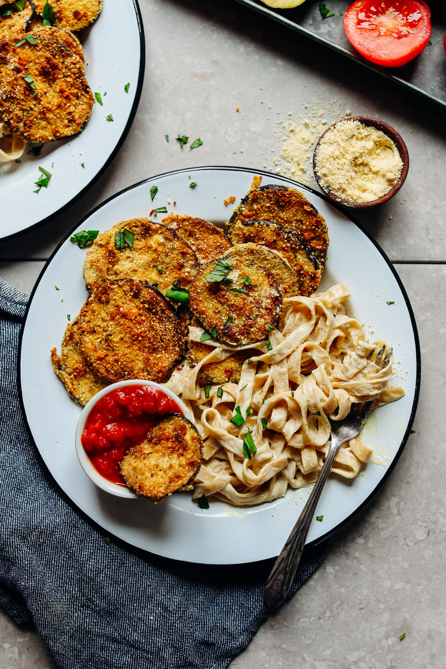 A big plate of gluten-free vegan comfort food including Crispy Eggplant Parmesan with marinara dipping sauce and a side of gluten-free pasta