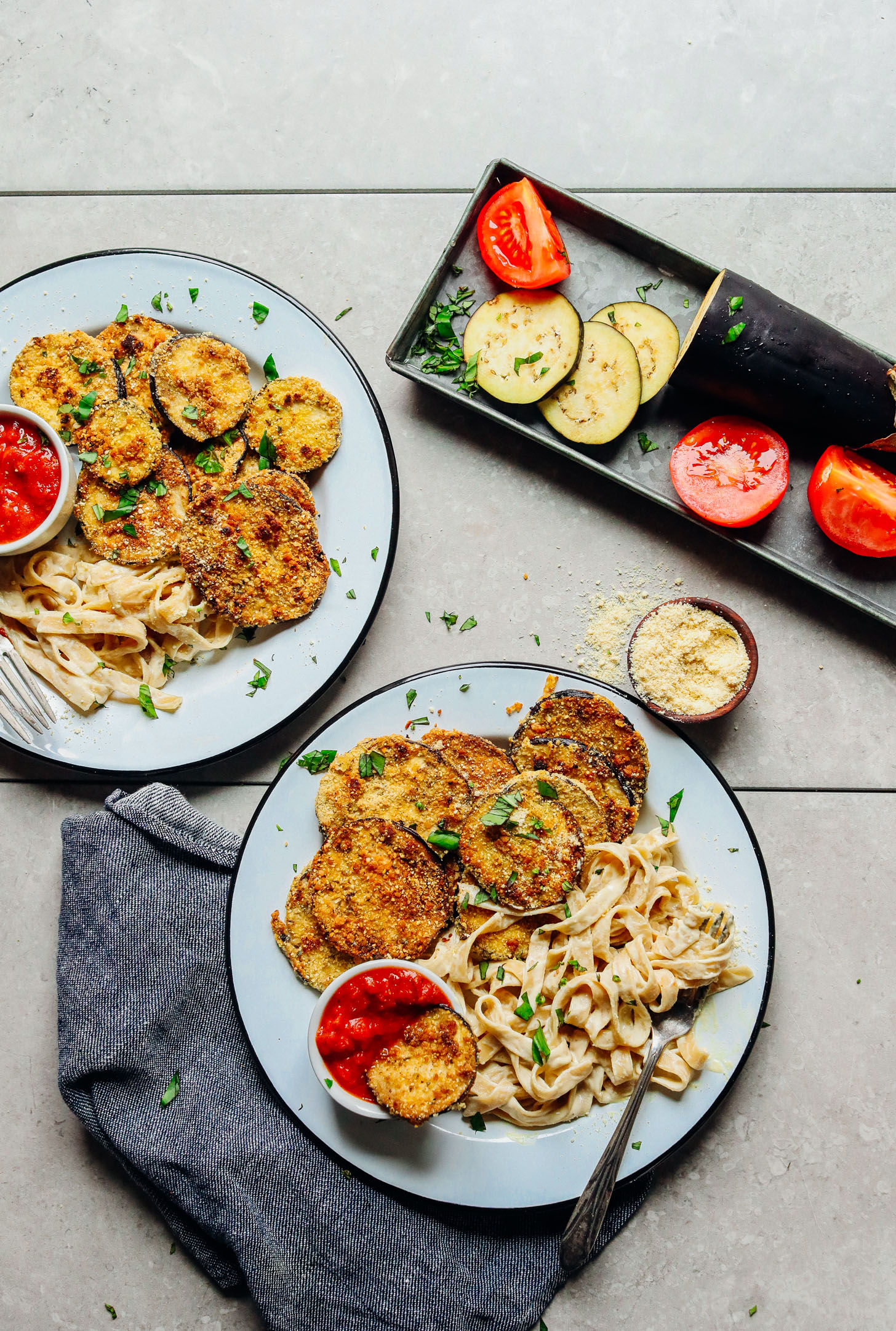 Two dinner plates served with Vegan Gluten Free Crispy Eggplant Parmesan alongside marinara dipping sauce and a helping of gluten-free pasta