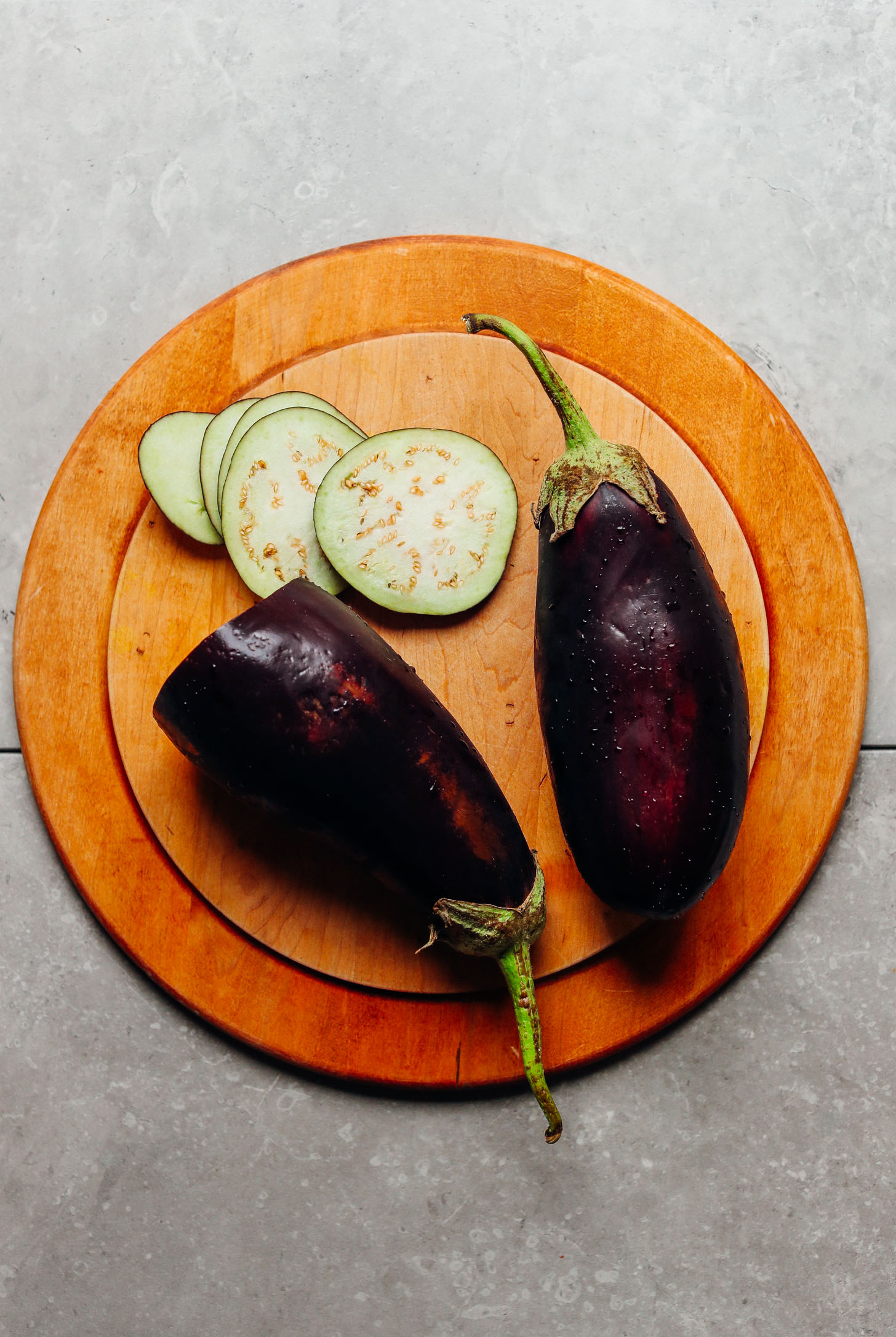 Whole and sliced eggplant on a wood cutting board