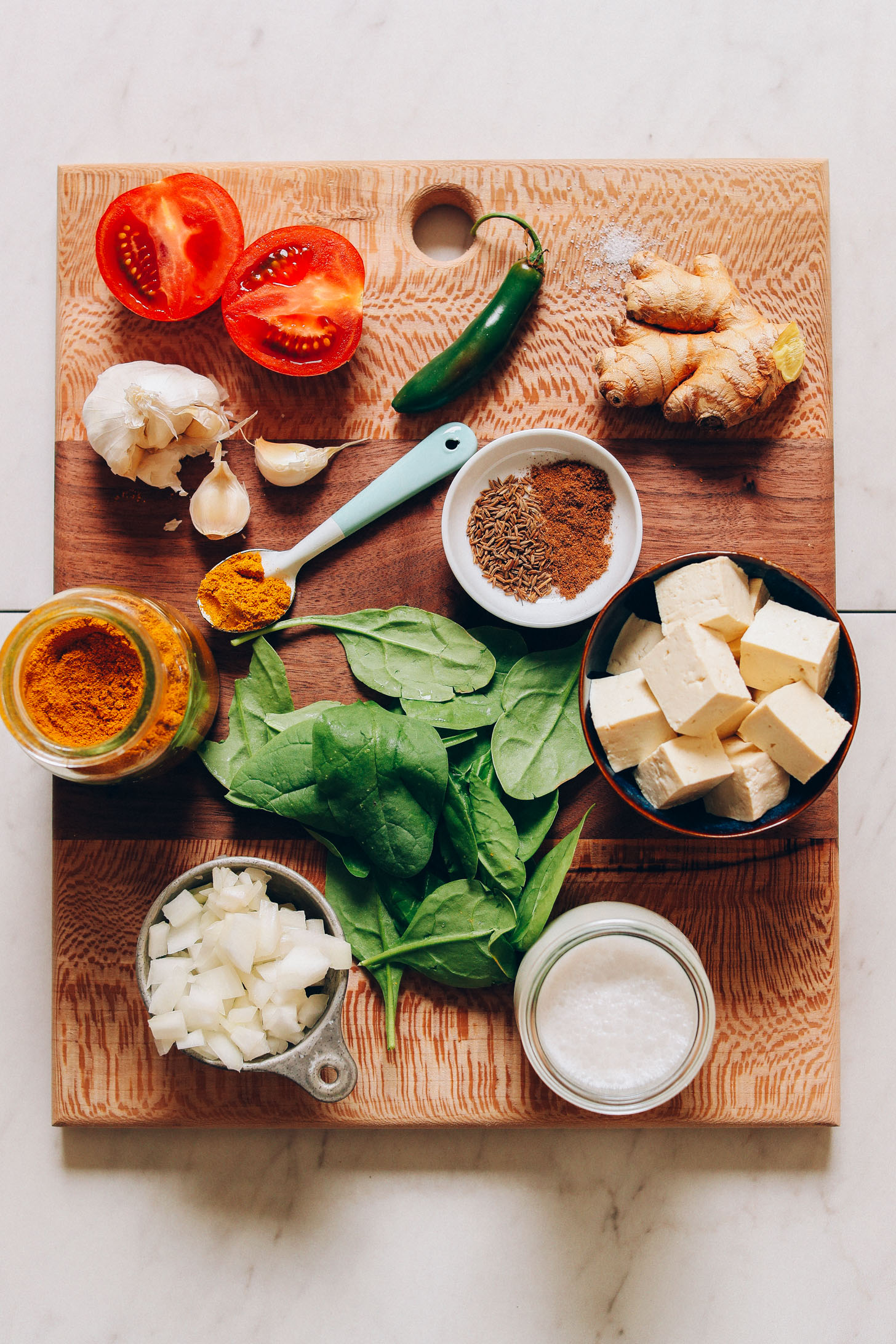 Overhead image of vegan palak paneer ingredients on a cutting board, including tomato, pepper, ginger, spinach, and tofu