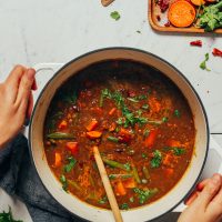 Holding the handles of a big pot of Spiced Sweet Potato Lentil Soup