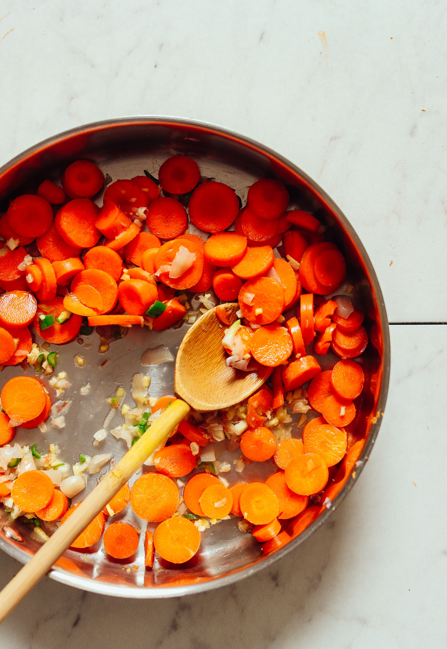 An overhead shot of sautéed carrots, shallot, ginger, garlic, and serrano pepper