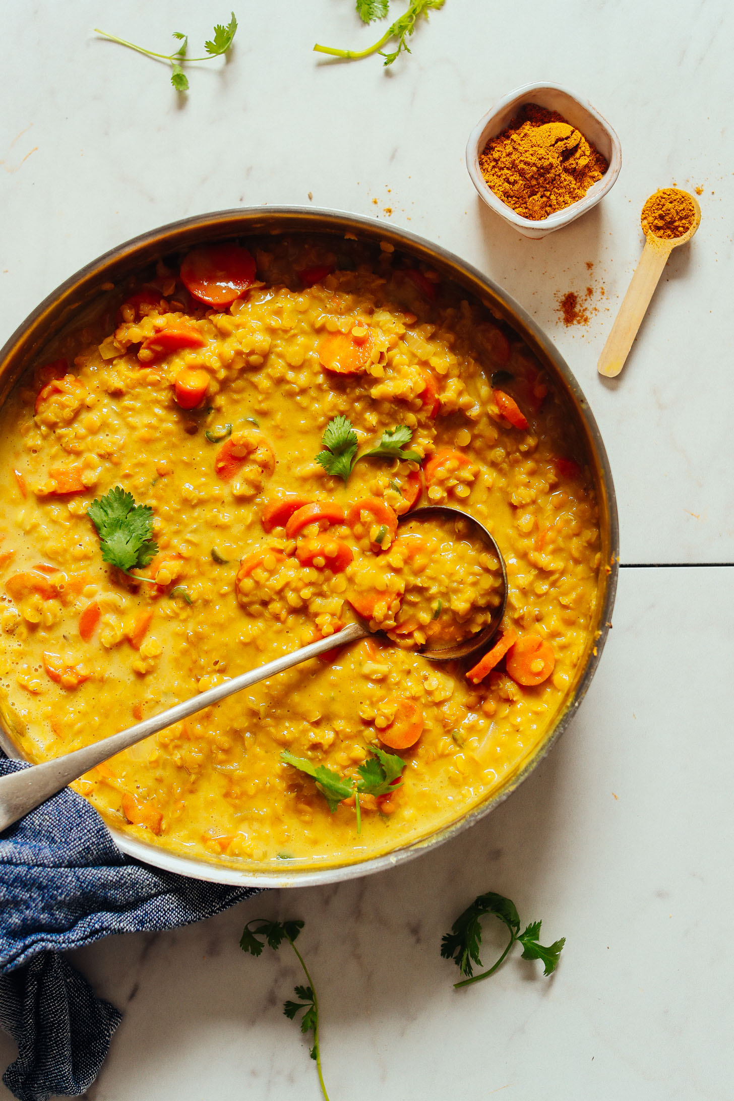 An overhead shot of golden curried lentil soup with a ladle and curry powder on the side.