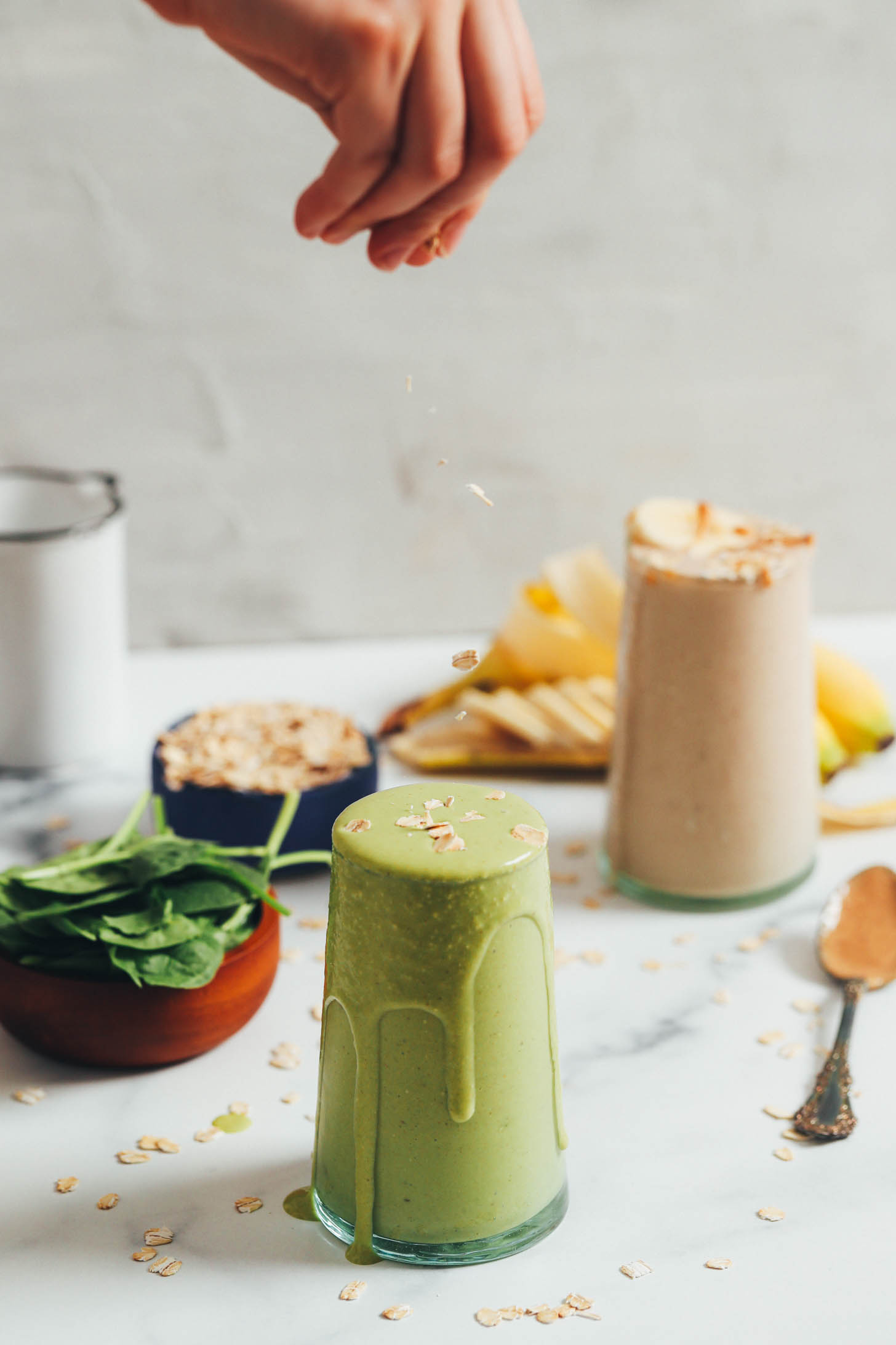 Sprinkling oats onto a green peanut butter banana smoothie