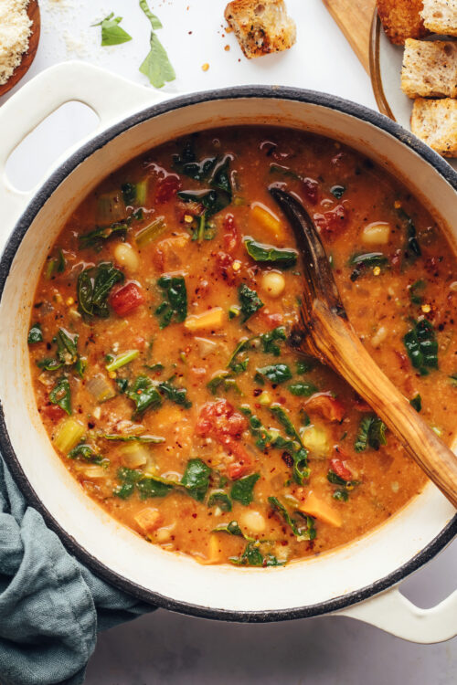 Using a wooden spoon to stir a pot of tuscan white bean and kale soup