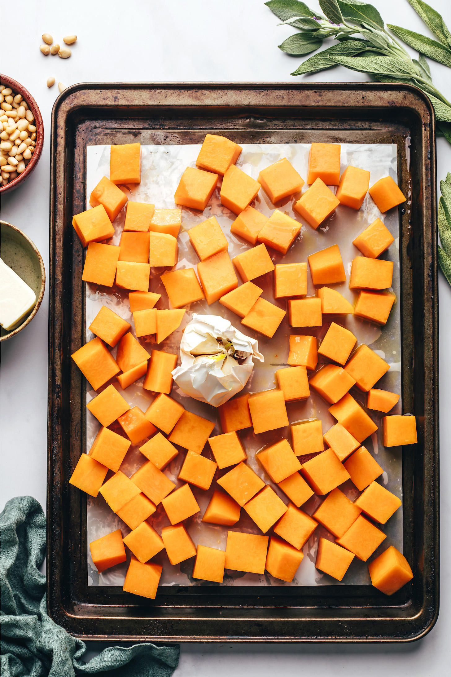 Cubed butternut squash and a head of garlic on a baking sheet