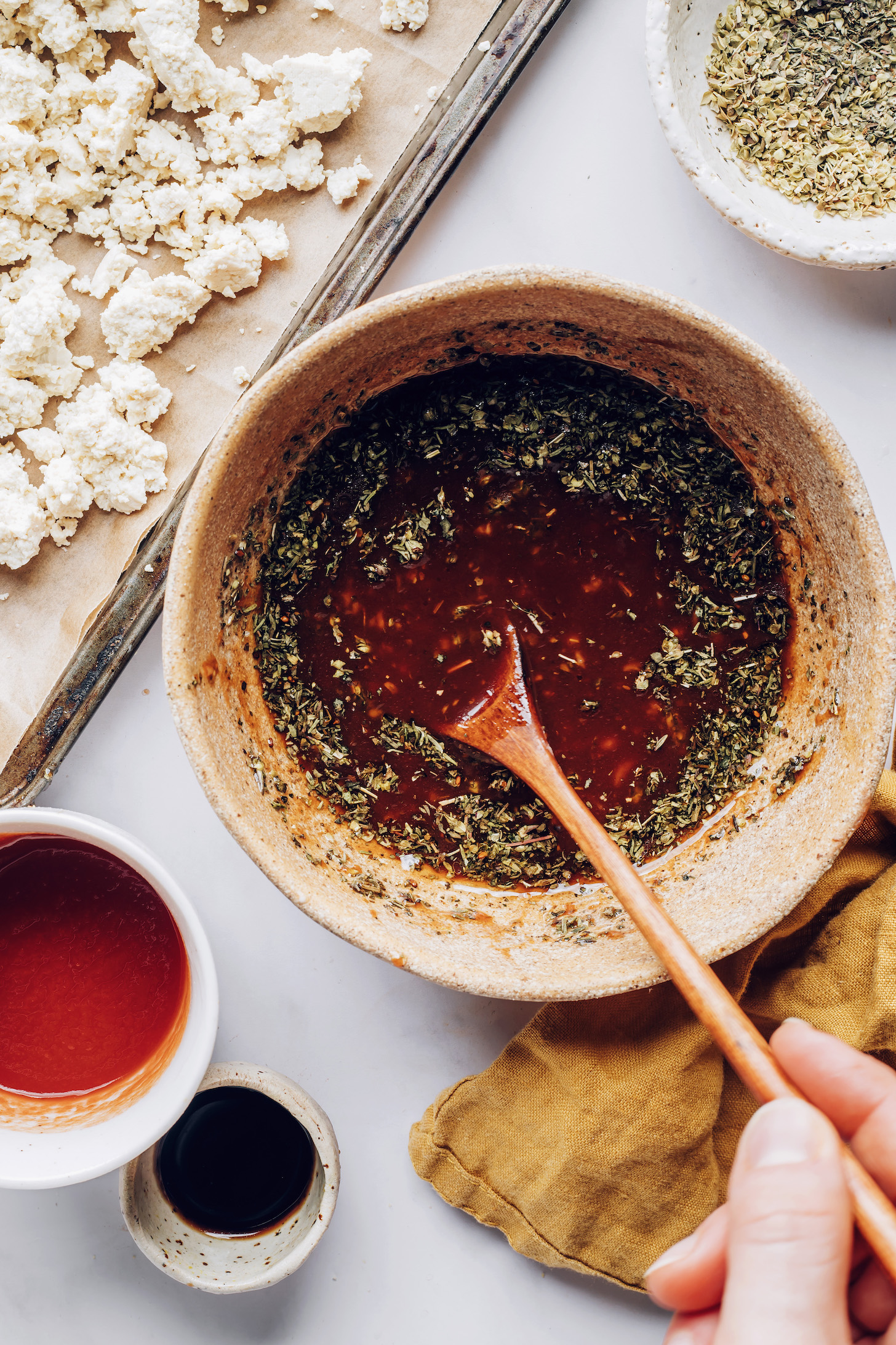 Crumbled tofu on a baking sheet next to a bowl of marinade