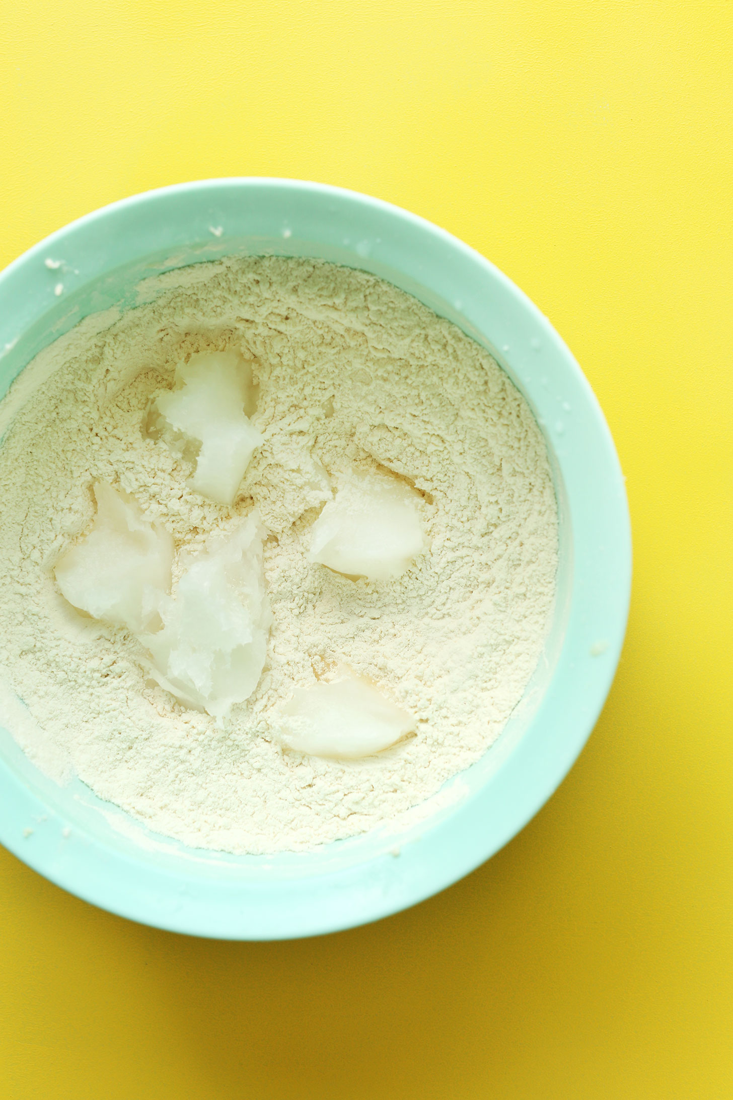 Mixing bowl of dry ingredients with chunks of coconut oil resting on top