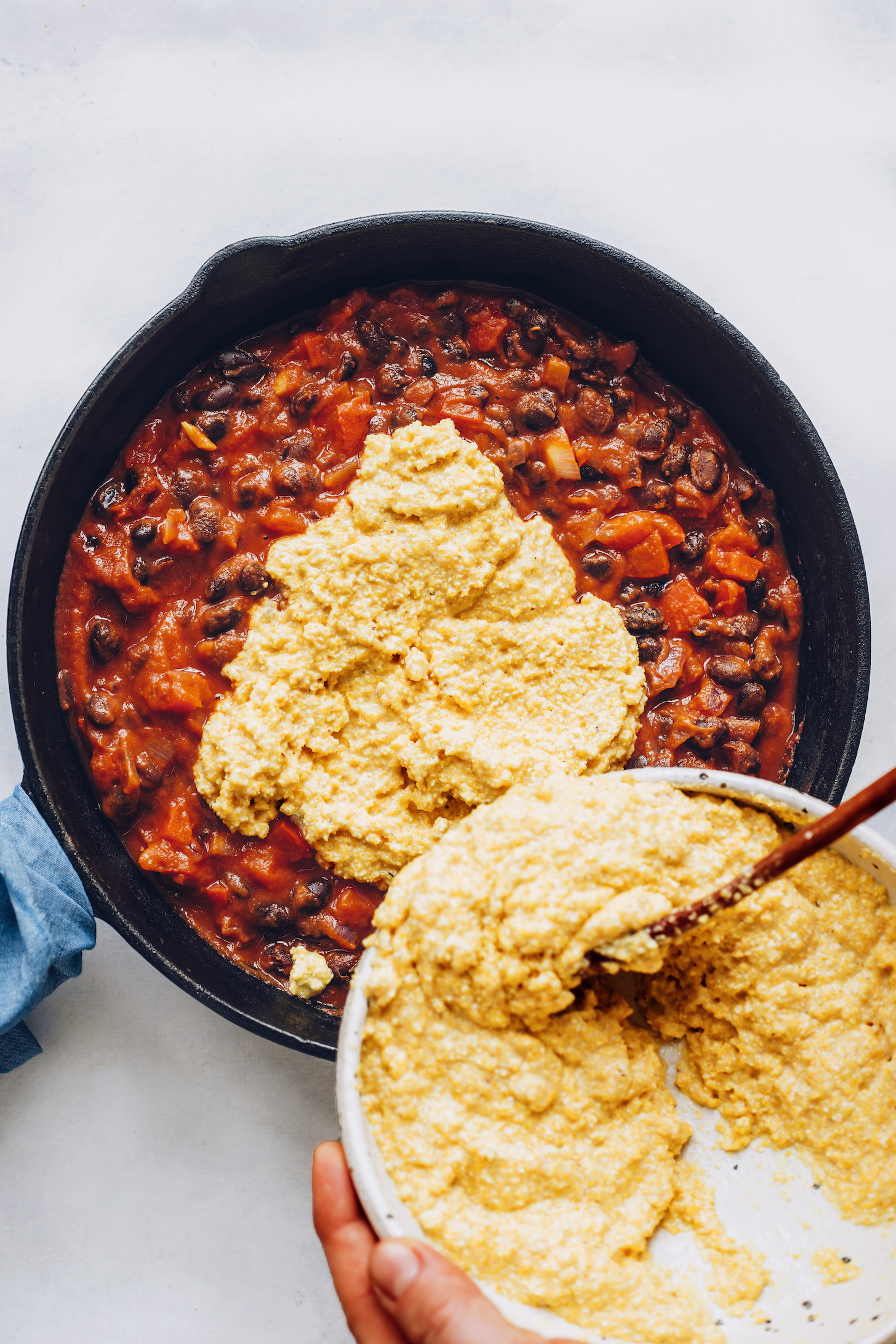 Pouring the cornbread layer over a skillet of our enchilada bake