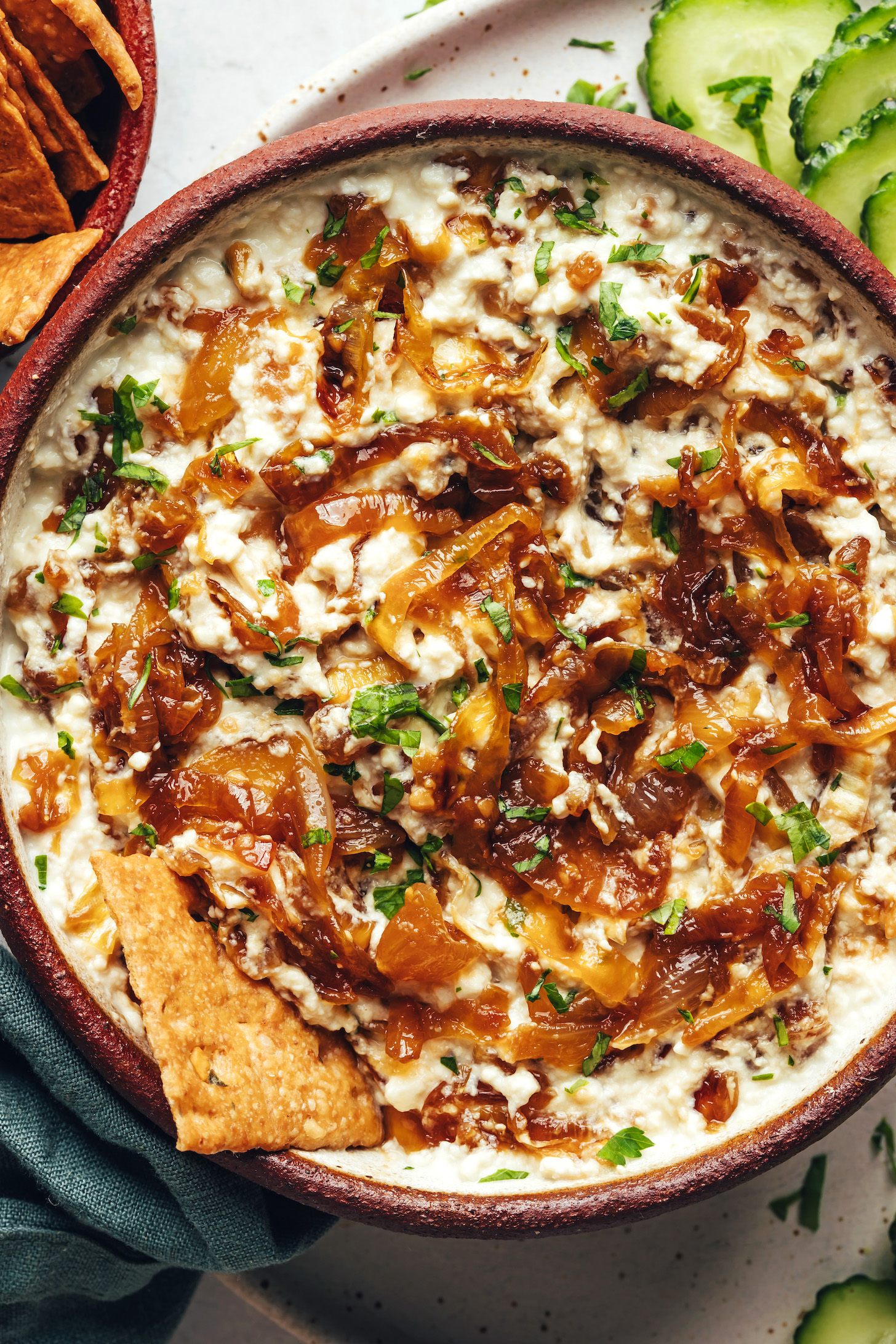 Sliced cucumbers and crackers next to a bowl of homemade caramelized onion dip