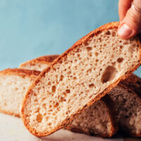 Holding up a slice of gluten-free artisan-style bread with more slices behind it