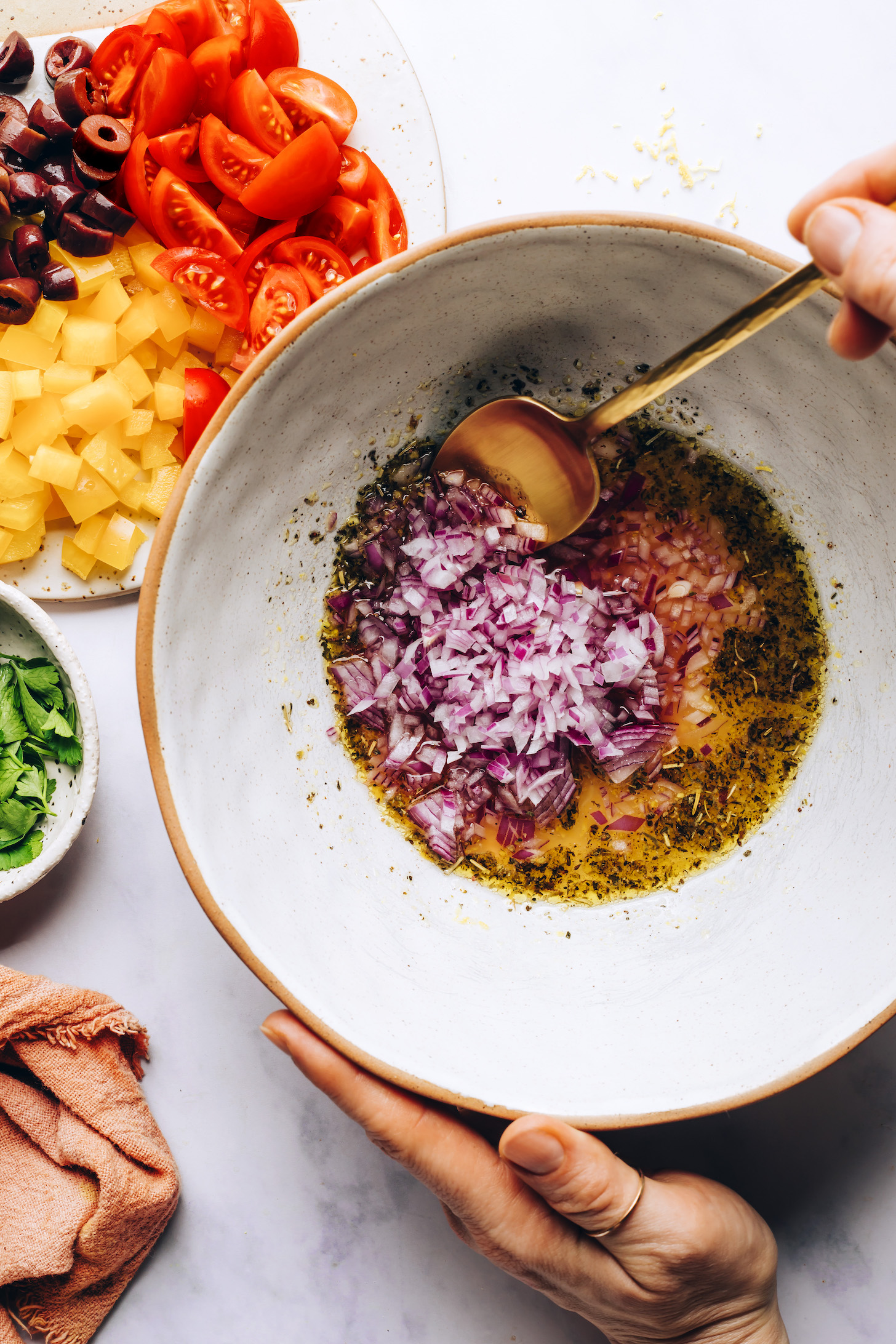 Fresh veggies beside a bowl of dressing with olive oil, red onion, dried herbs, and other ingredients