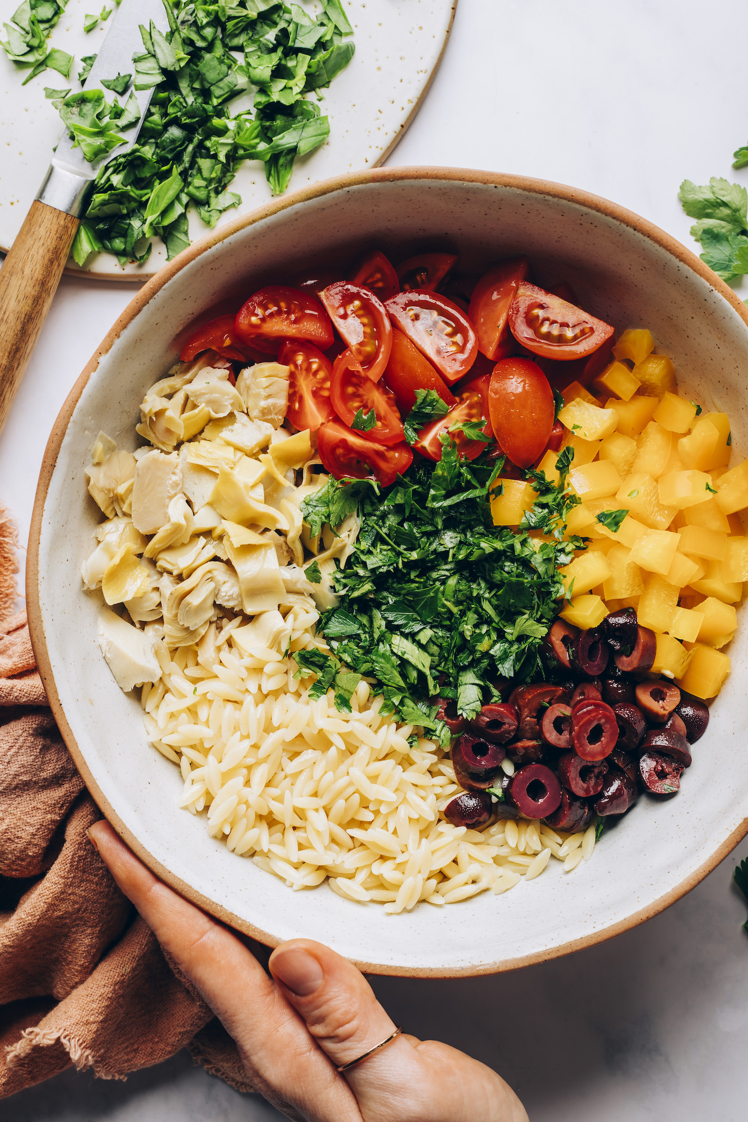 Bowl of fresh tomatoes, bell pepper, parsley, artichoke hearts, kalamata olives, and orzo pasta