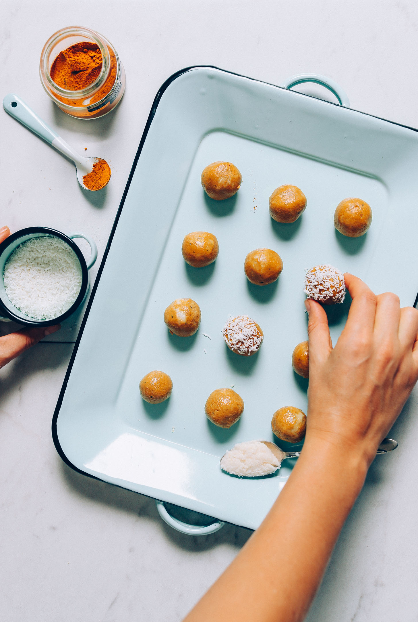 An overhead image of golden milk snack balls being dipped in shredded coconut with a dish of turmeric on the side