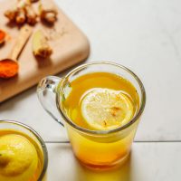 image of lemon ginger water at a 45 degree angle in a clear mug with spoonfuls of spices behind it