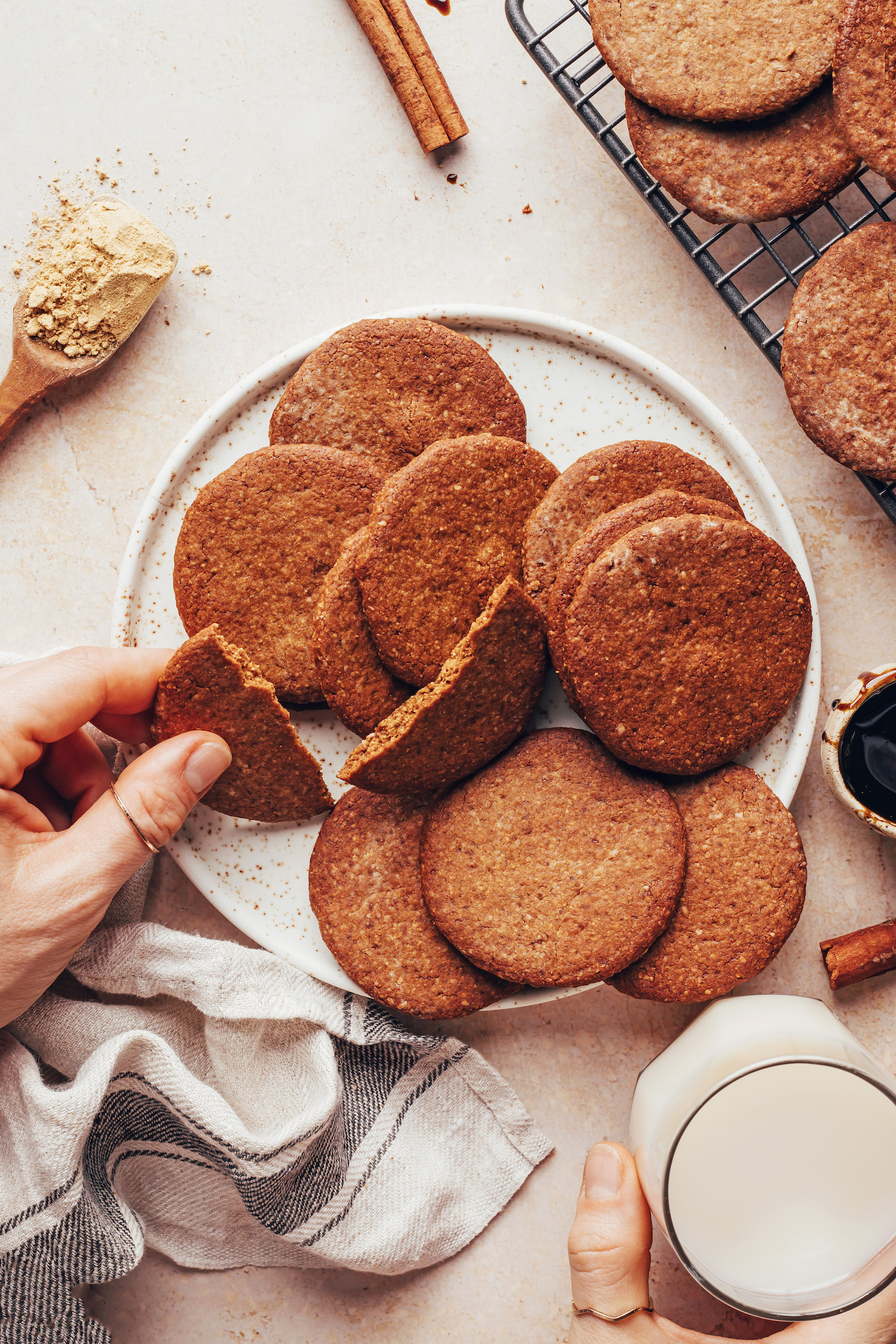 Picking up half of a snapped gingersnap cookie from a plate of more cookies