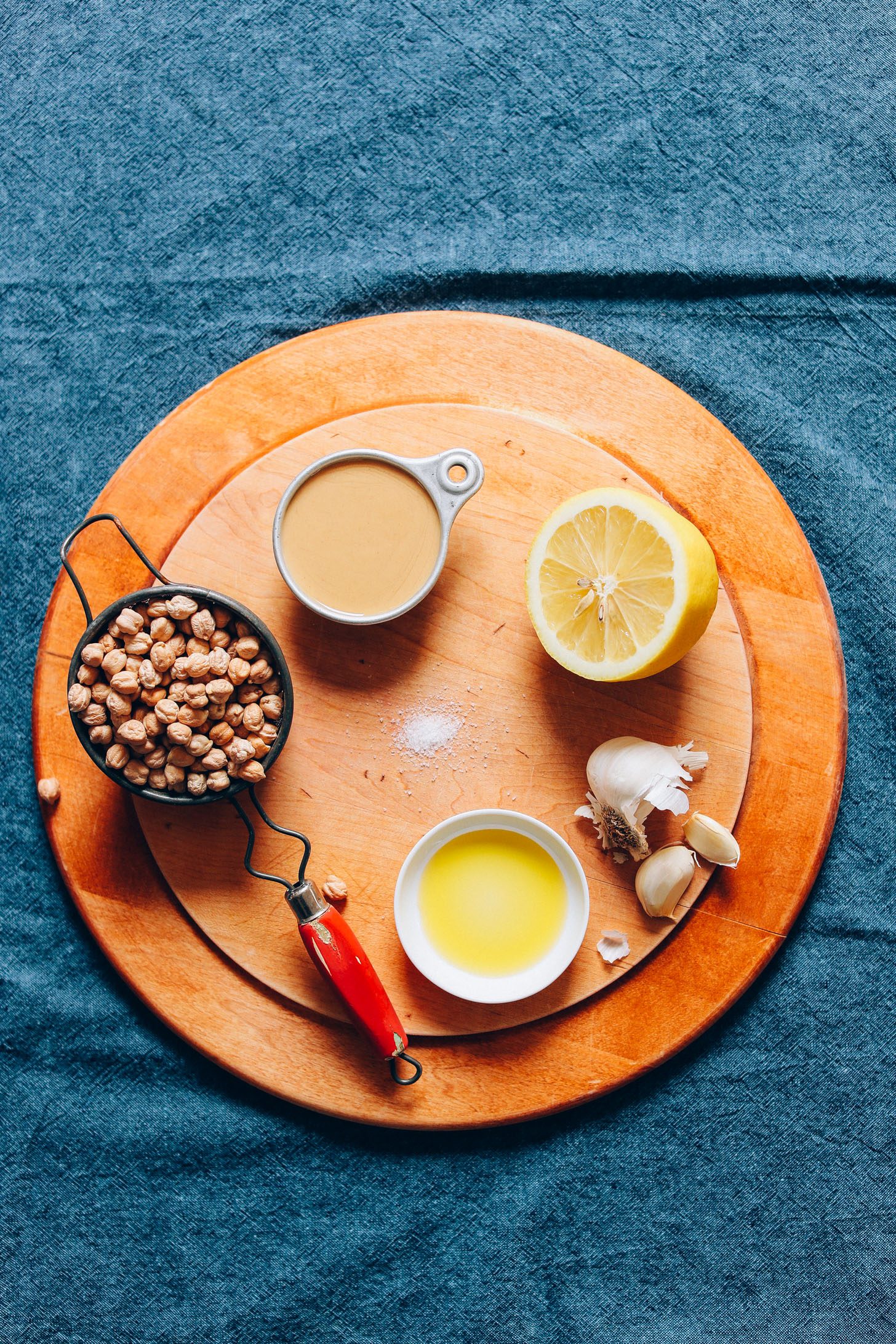 Wood cutting board with chickpeas, tahini, olive oil, garlic, lemon, and salt for making perfect hummus from scratch