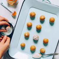 Coating a Golden Milk Snack Bite in shredded coconut beside a tray with more bites