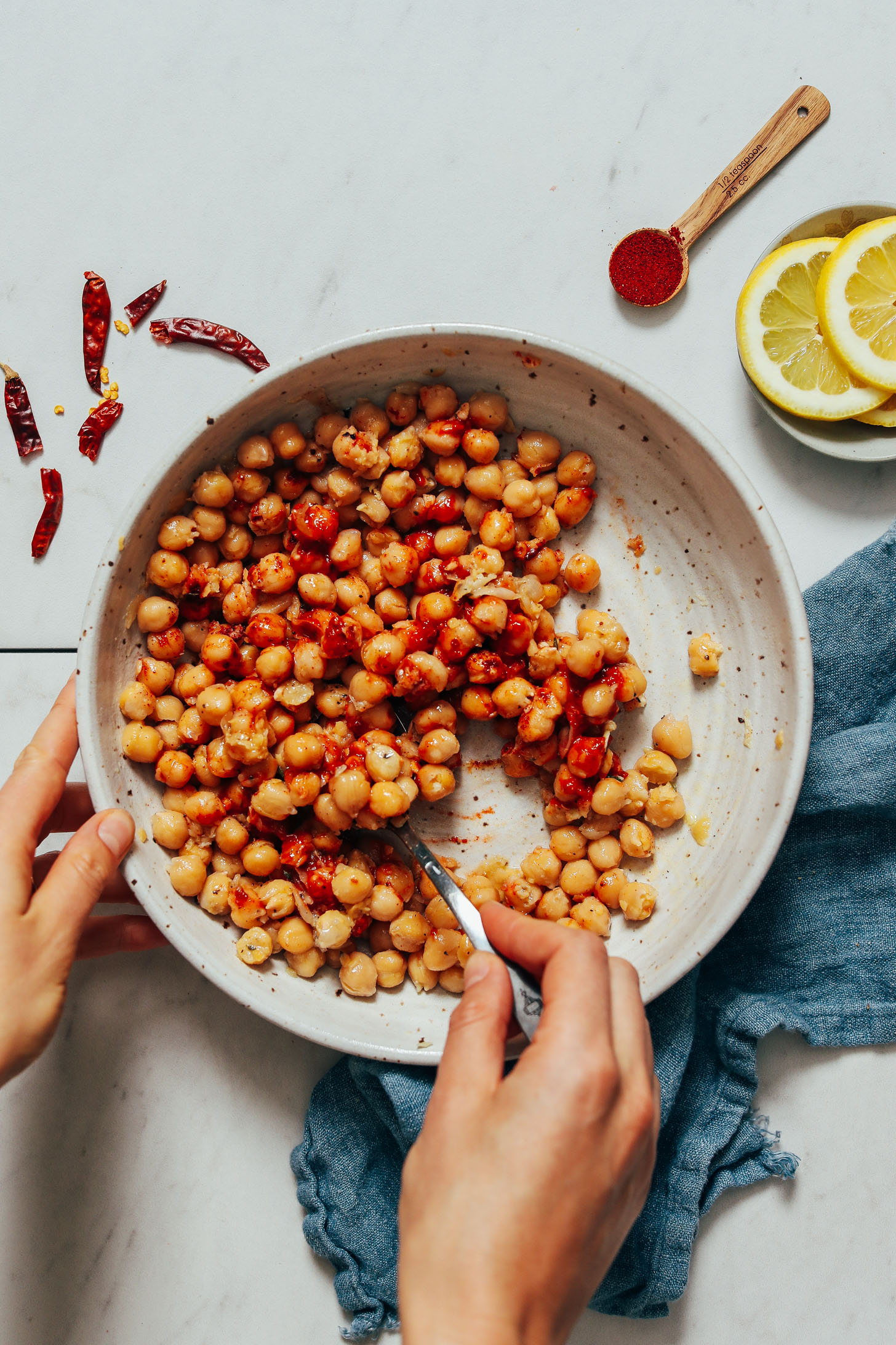 Using a spoon to stir together chickpeas, harissa paste, lemon juice, garlic, sea salt, maple syrup, smoked paprika, and olive oil