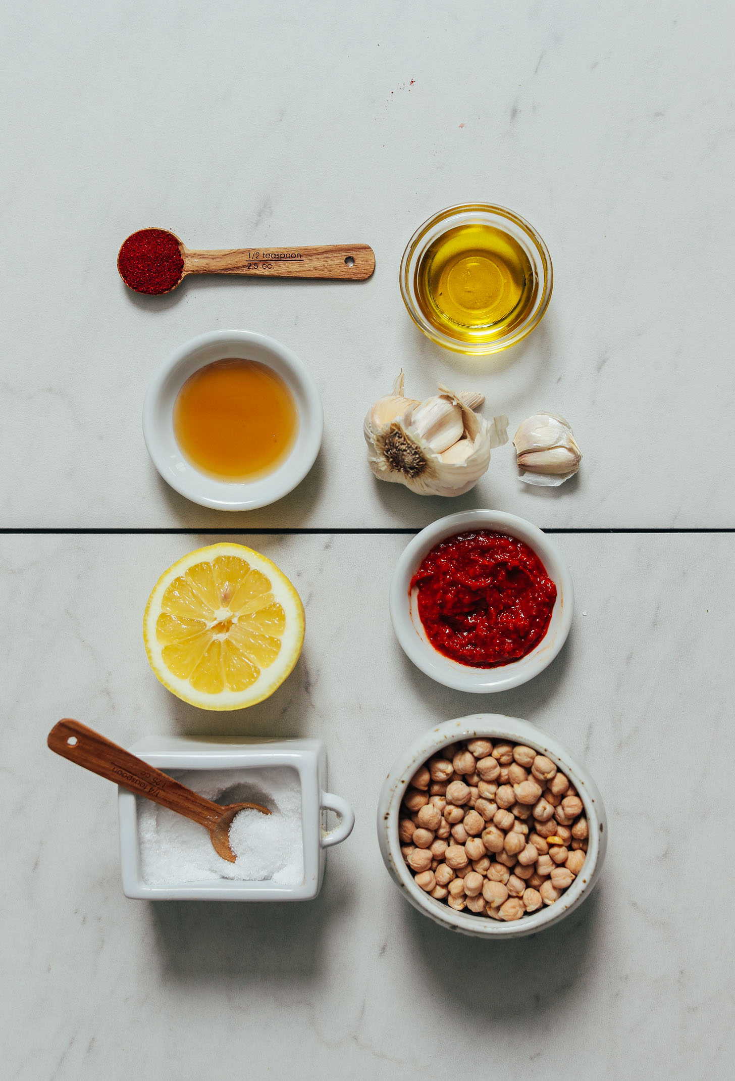 Spoons and dishes or salt, lemon juice, maple syrup, paprika, olive oil, garlic, harissa paste, and dry chickpeas