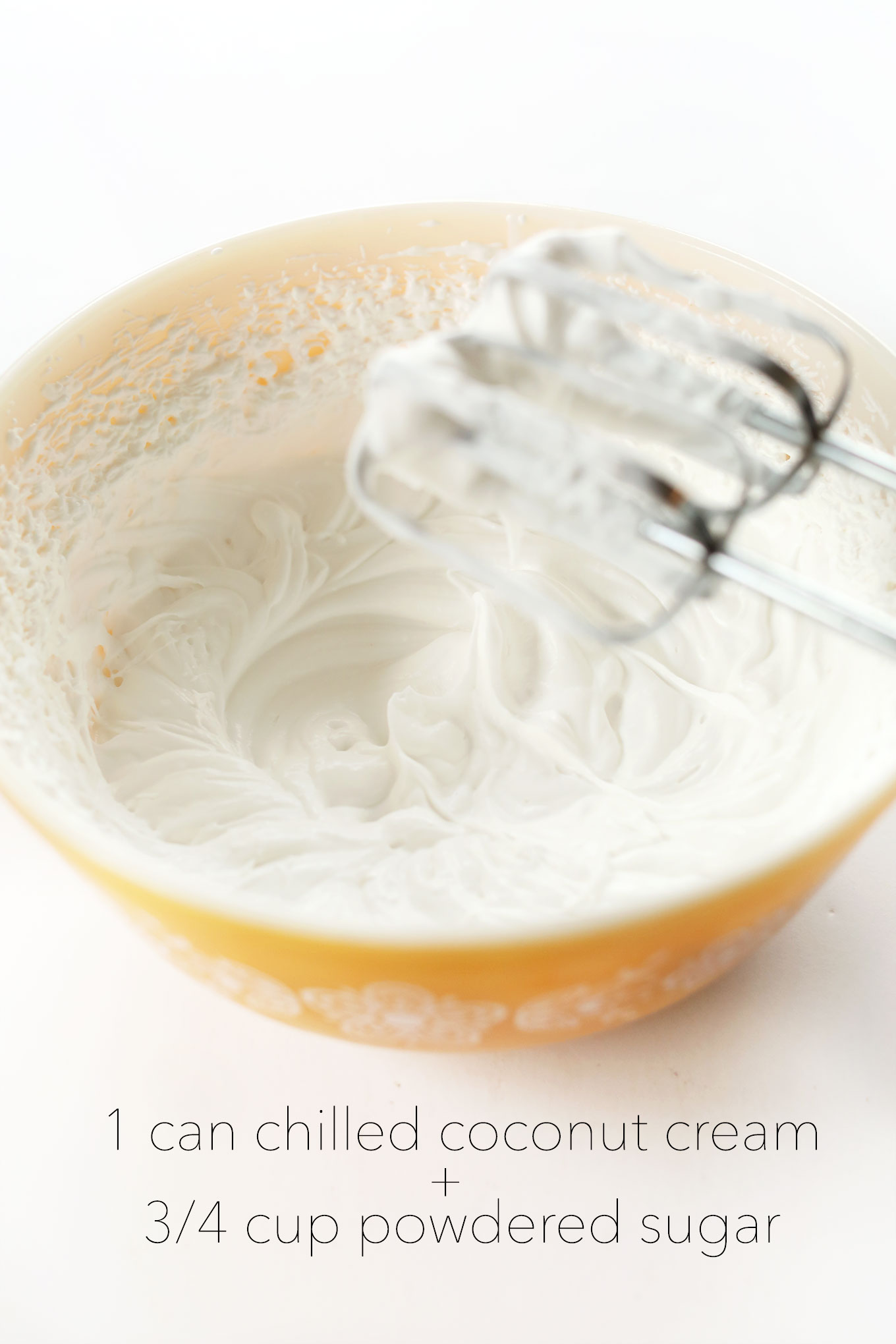 Electric mixer resting above a bowl of fluffy homemade Coconut Whipped Cream