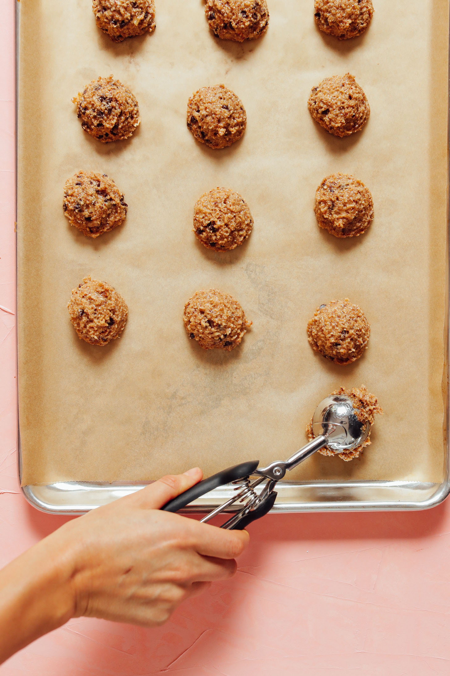 Using a small ice cream scooper to place Banana Chocolate Chip Cookie dough batter onto a baking sheet