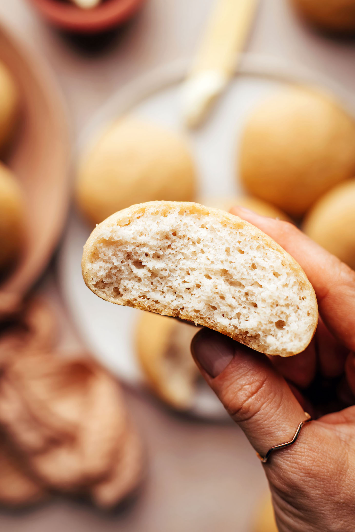 Hand holding up a vegan gluten-free dinner roll to show the inner texture