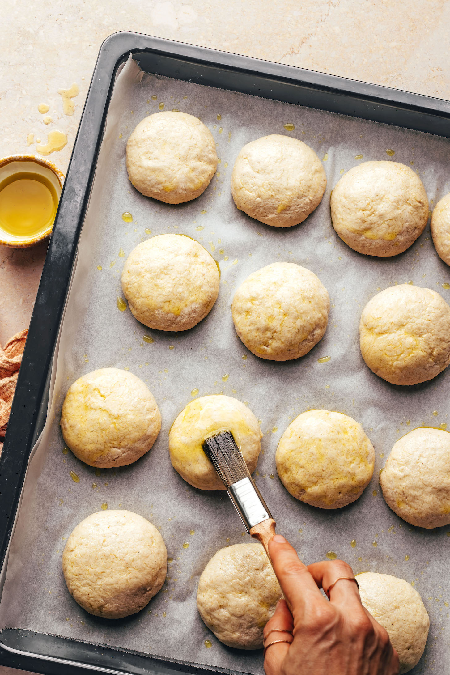 Brushing vegan gluten-free dinner rolls with olive oil