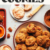 Plate of fluffy 1-bowl pumpkin oat cookies next to a bowl of frosting and some frosted cookies