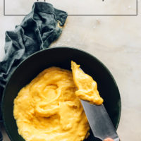 Using a knife to pick up vegan cheddar cheese from a bowl