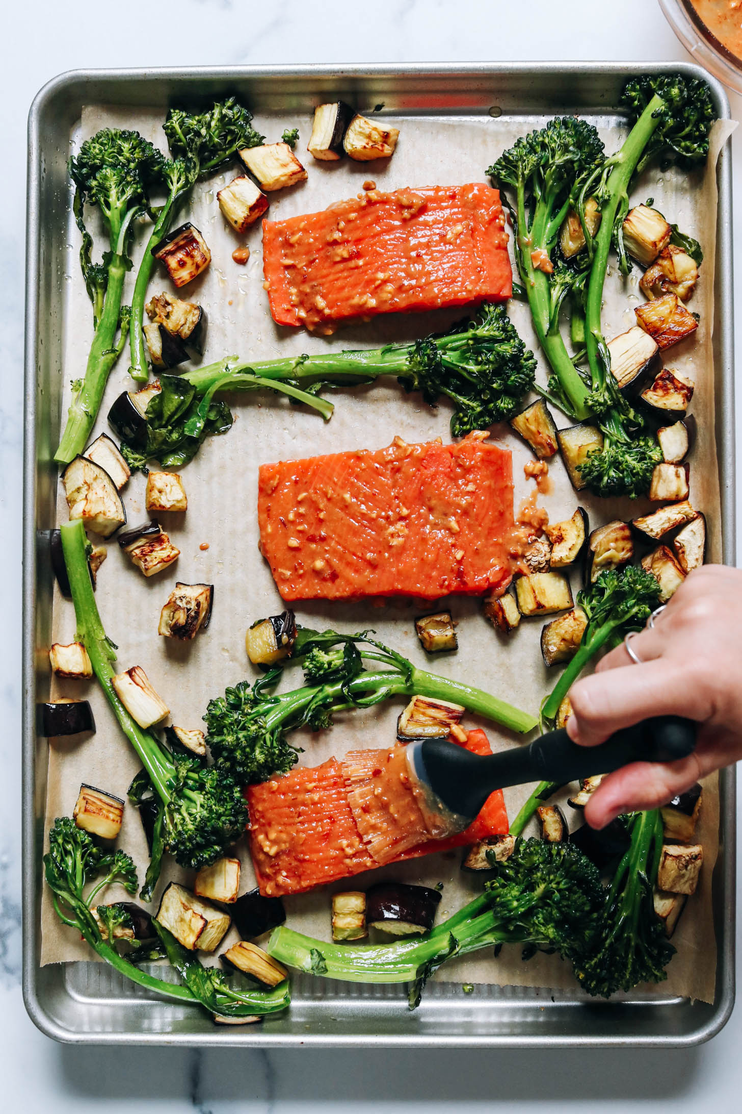 Brushing a miso glaze onto salmon on a sheet pan