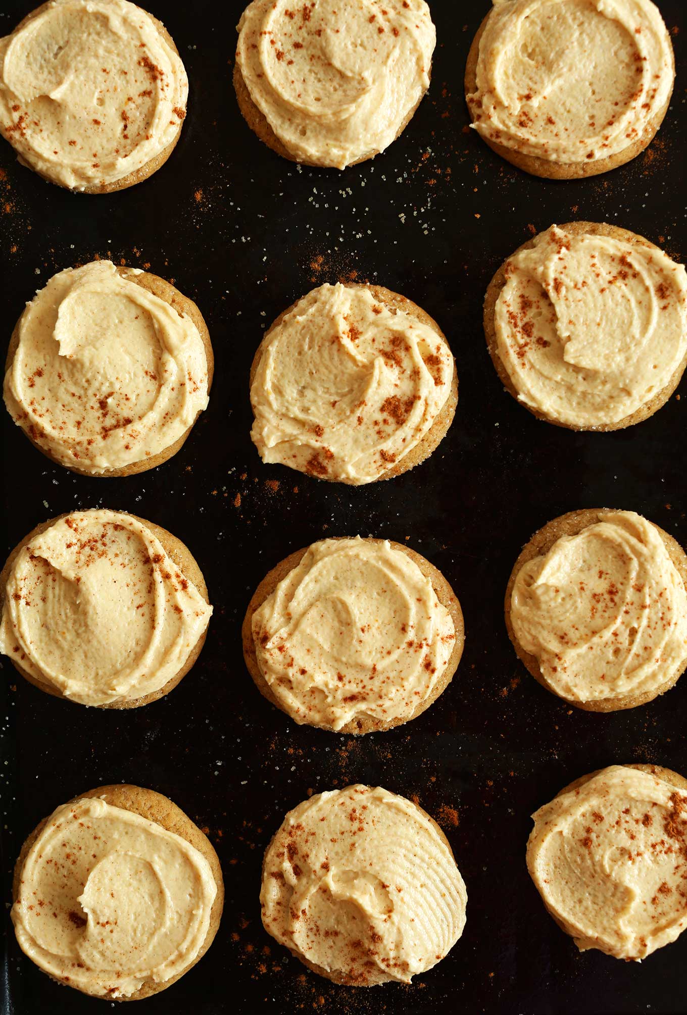 Baking sheet with freshly frosted Vegan Pumpkin Sugar Cookies topped with pumpkin pie spice