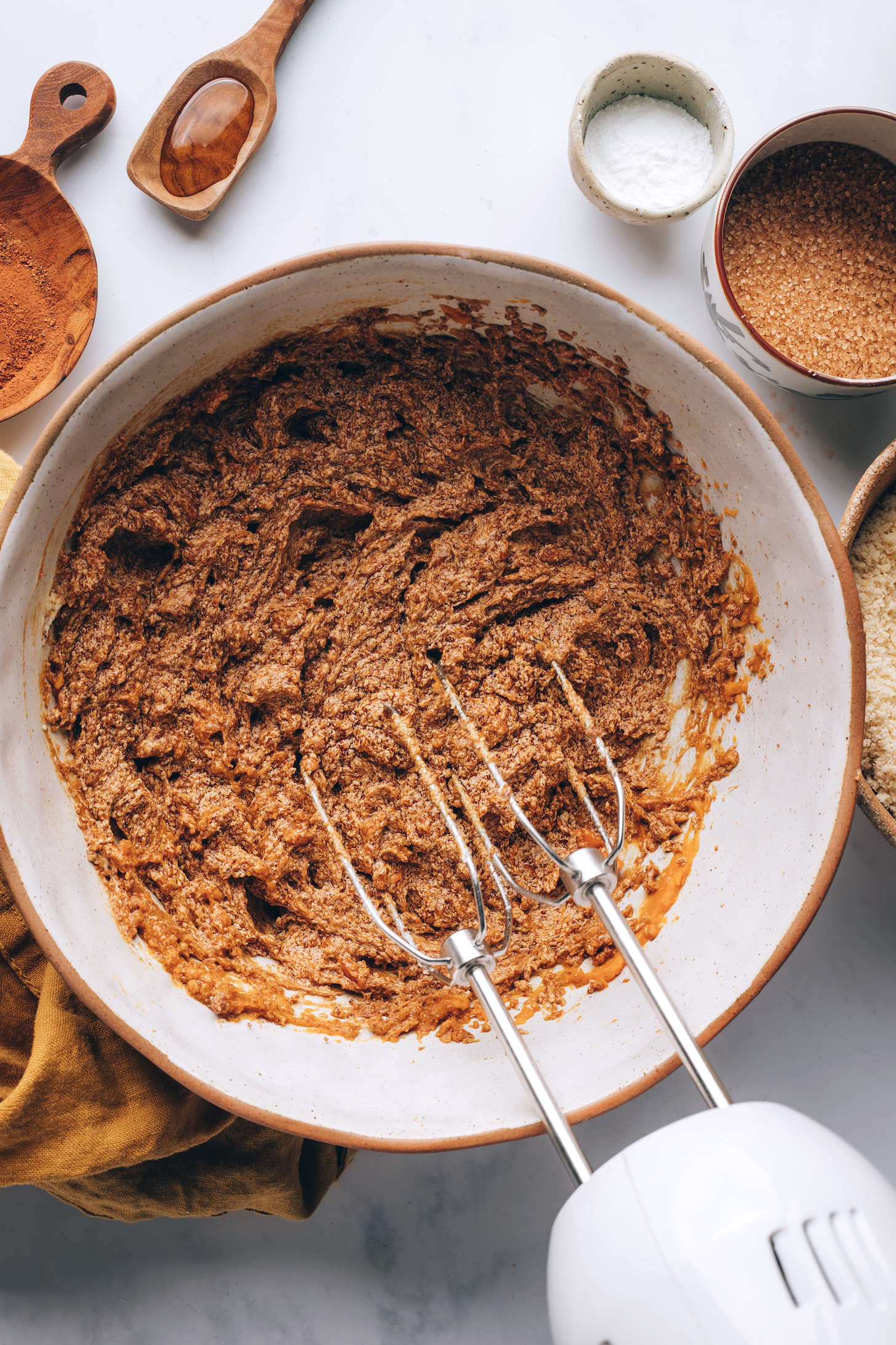 Hand mixer over a bowl of whipped vegan butter, coconut sugar, vanilla, and pumpkin purée