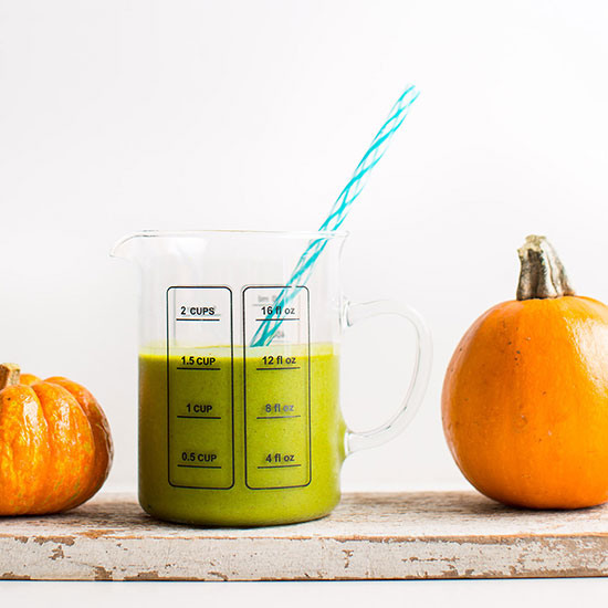 Pumpkins on a wood plank beside a measuring glass of our Pumpkin Pie Green Smoothie recipe