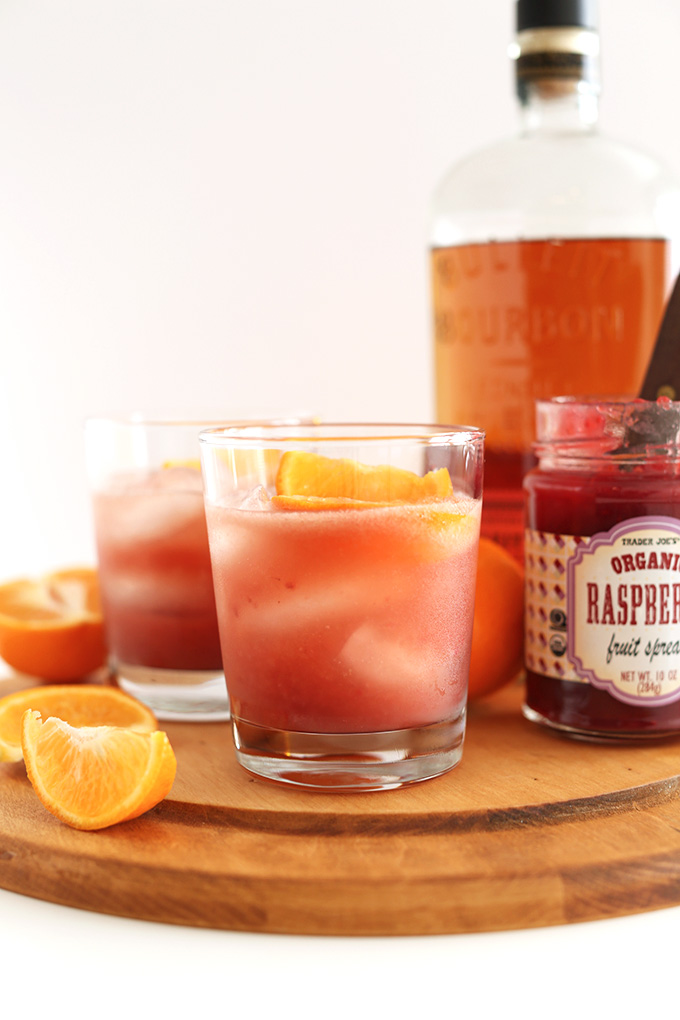 Glasses of our Raspberry Jam Bourbon Smash recipe surrounded by ingredients used to make it