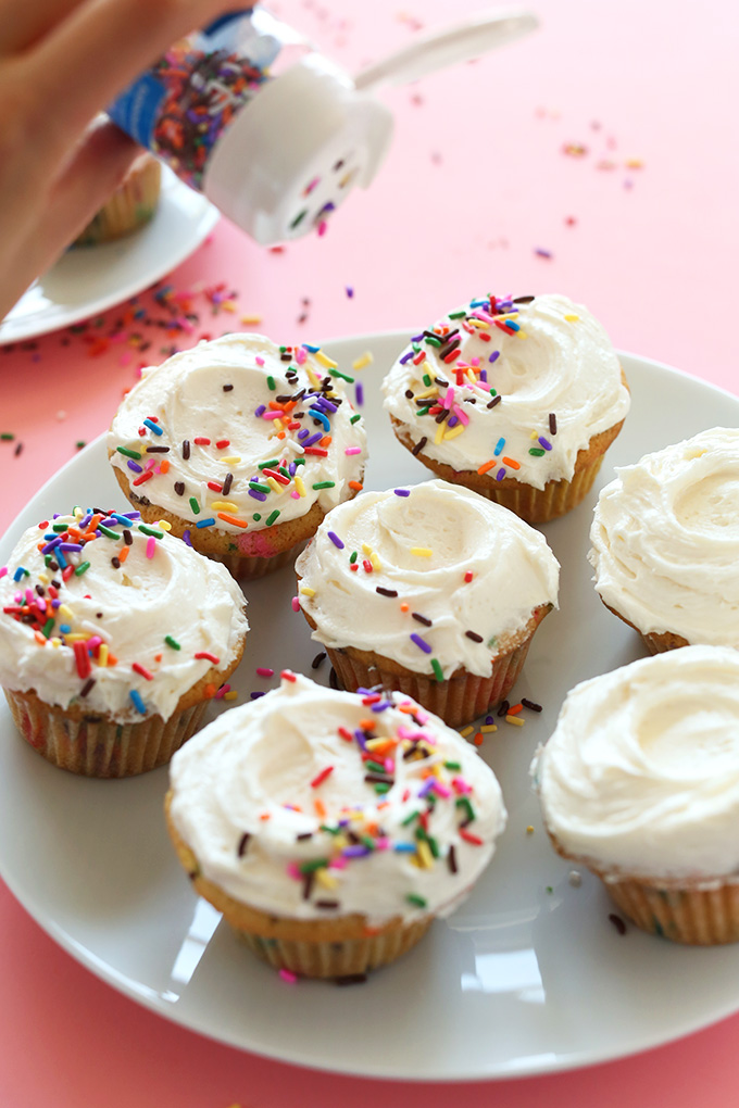 Adding sprinkles to frosted Vegan Funfetti Cupcakes