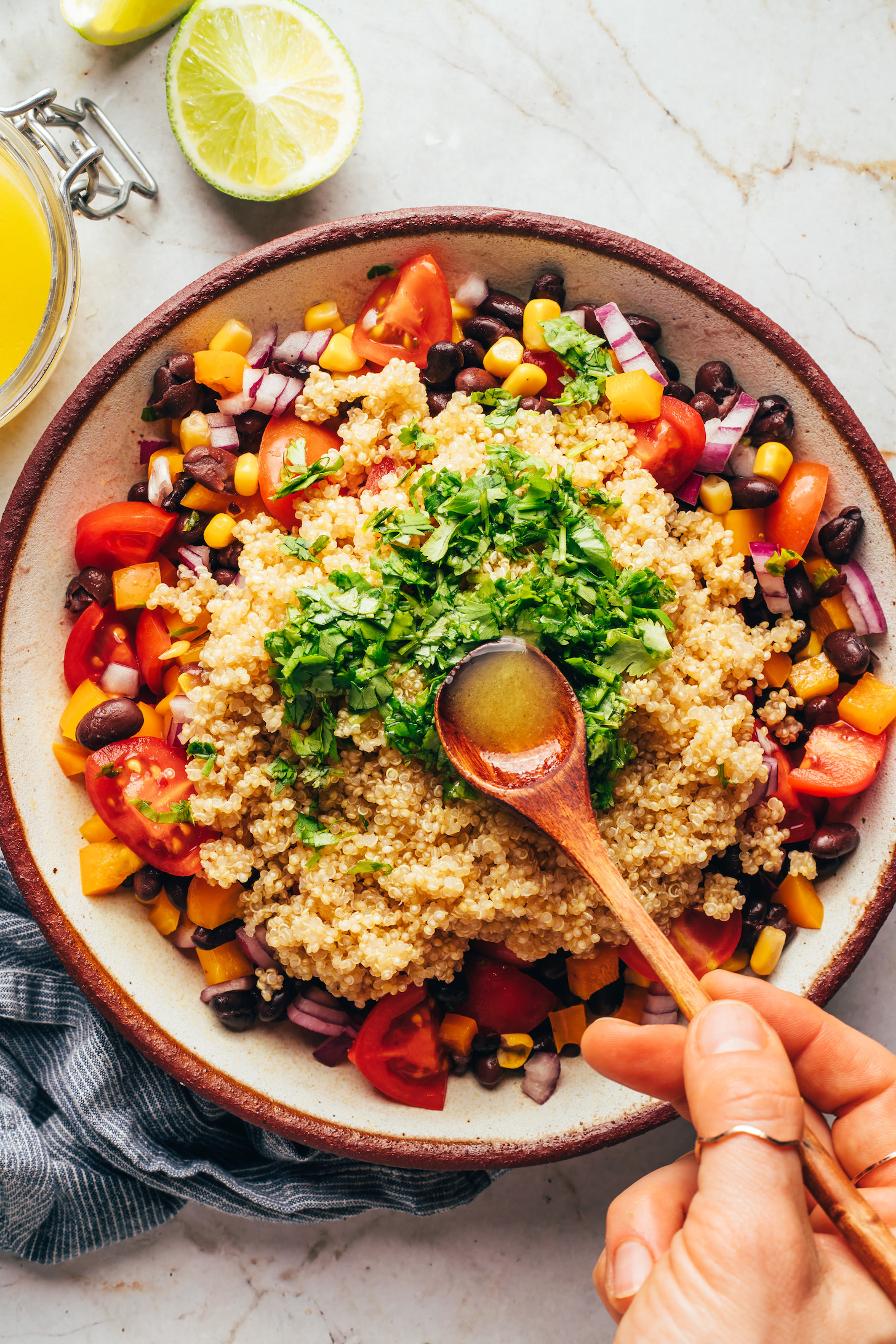 Pouring a lime vinaigrette over fresh cilantro, quinoa, and vegetables