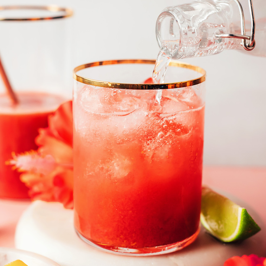 Pouring sparkling water over a hibiscus orange mango mixture in a glass